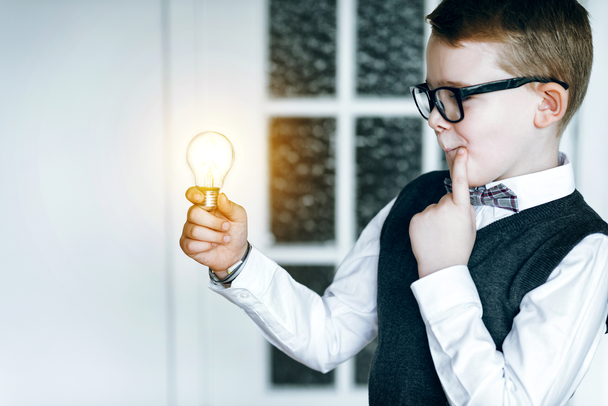 light bulb glows while boy with glasses gets an idea