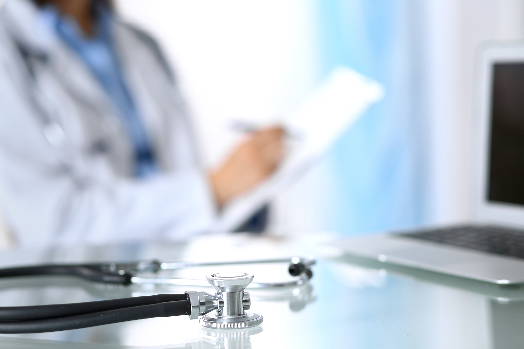 stethoscope lying on glass desk with laptop computer at busy phy