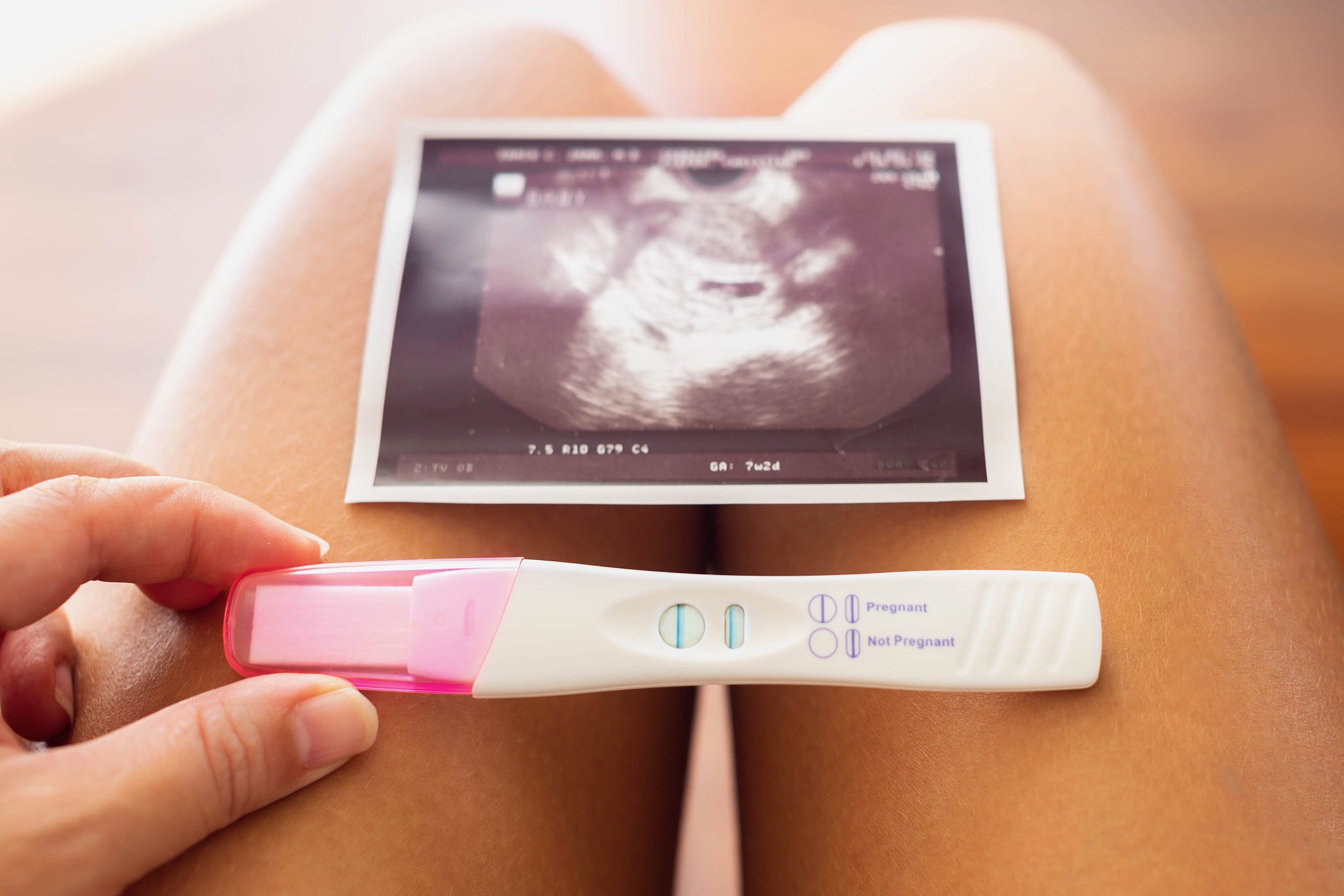 a woman holding a pregnancy test and a photo of the baby. planni