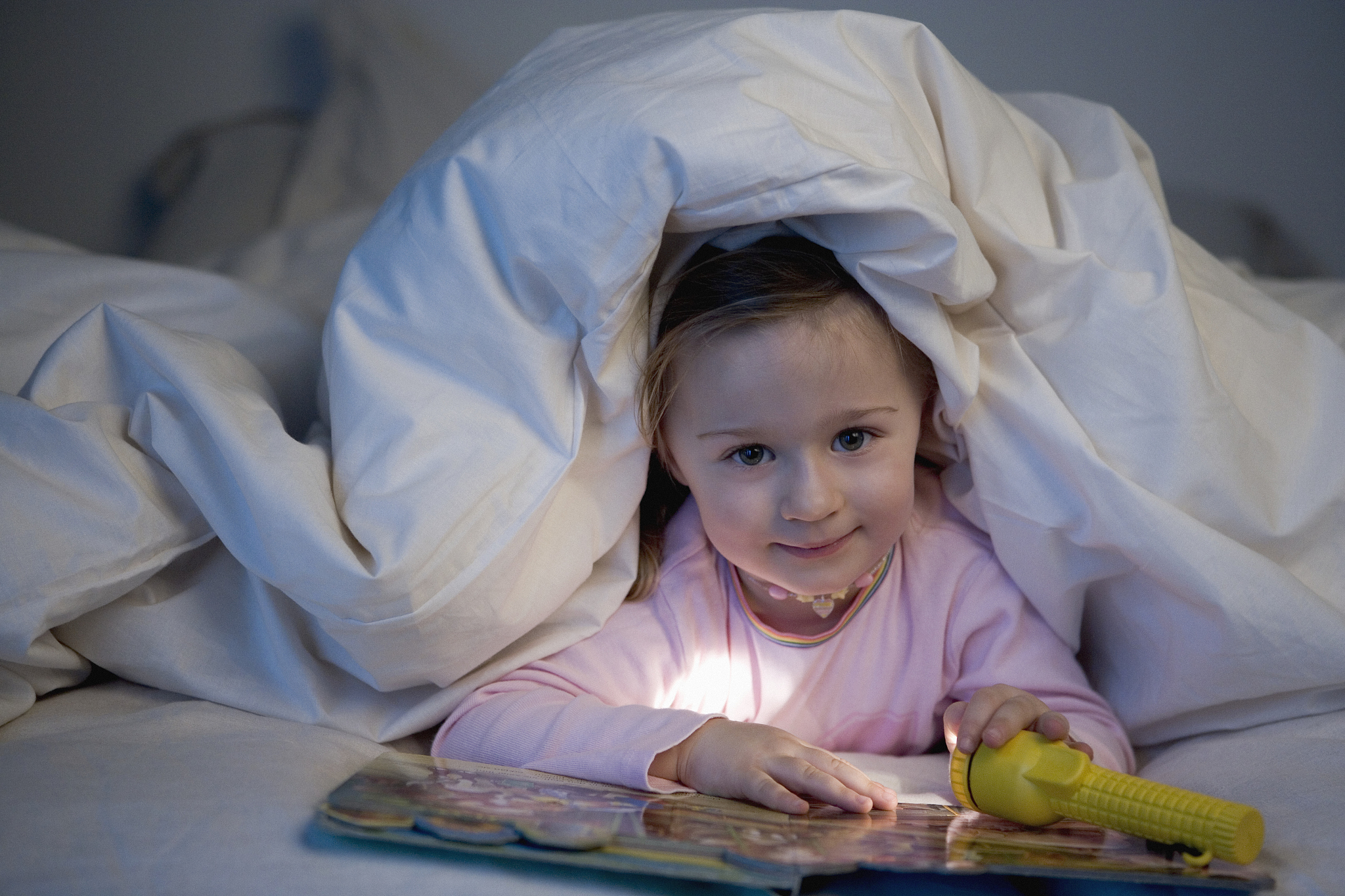 girl holding torch and reading book in bed