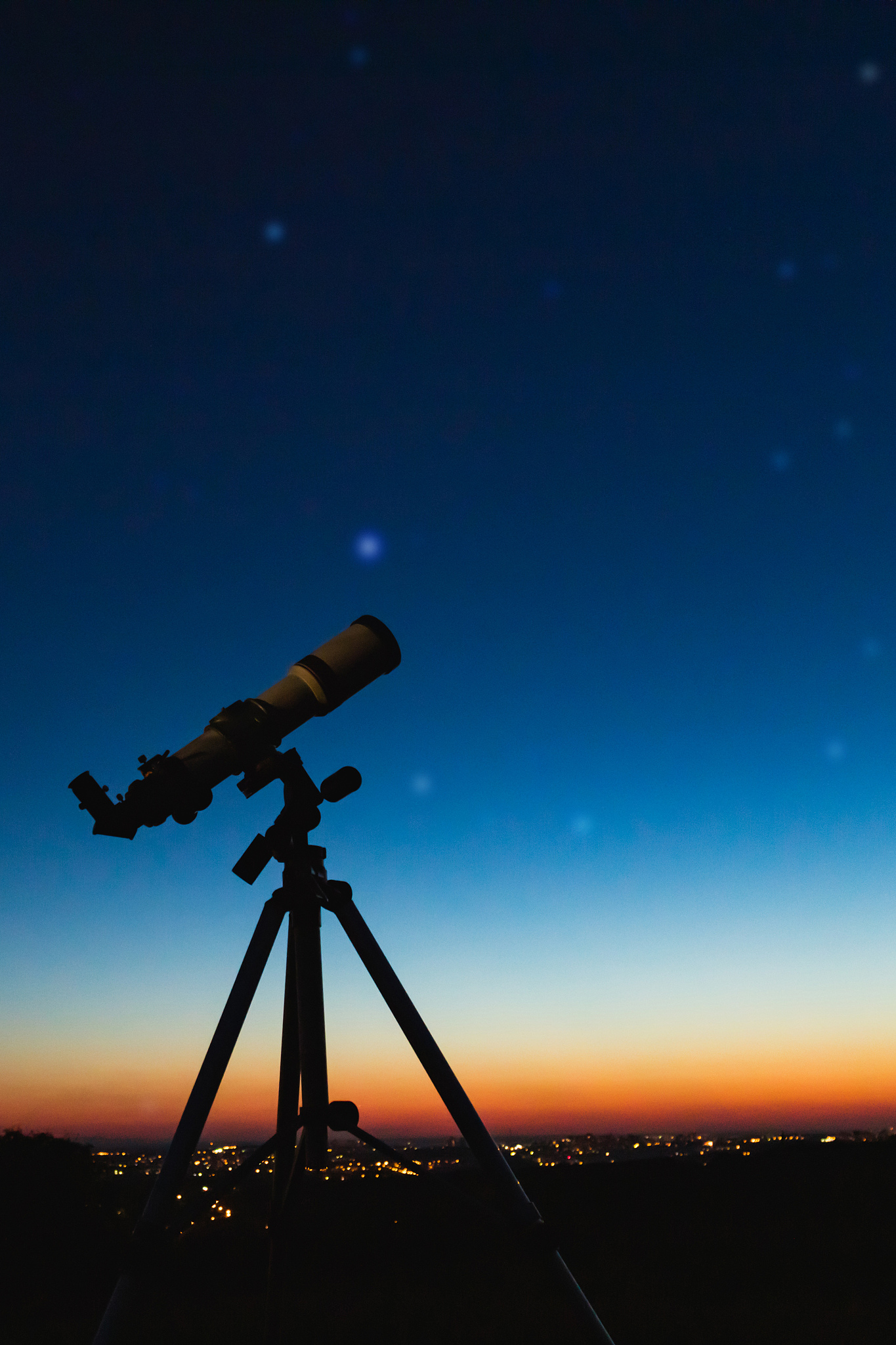 telescope silhouette and night sky with city lights in the backg
