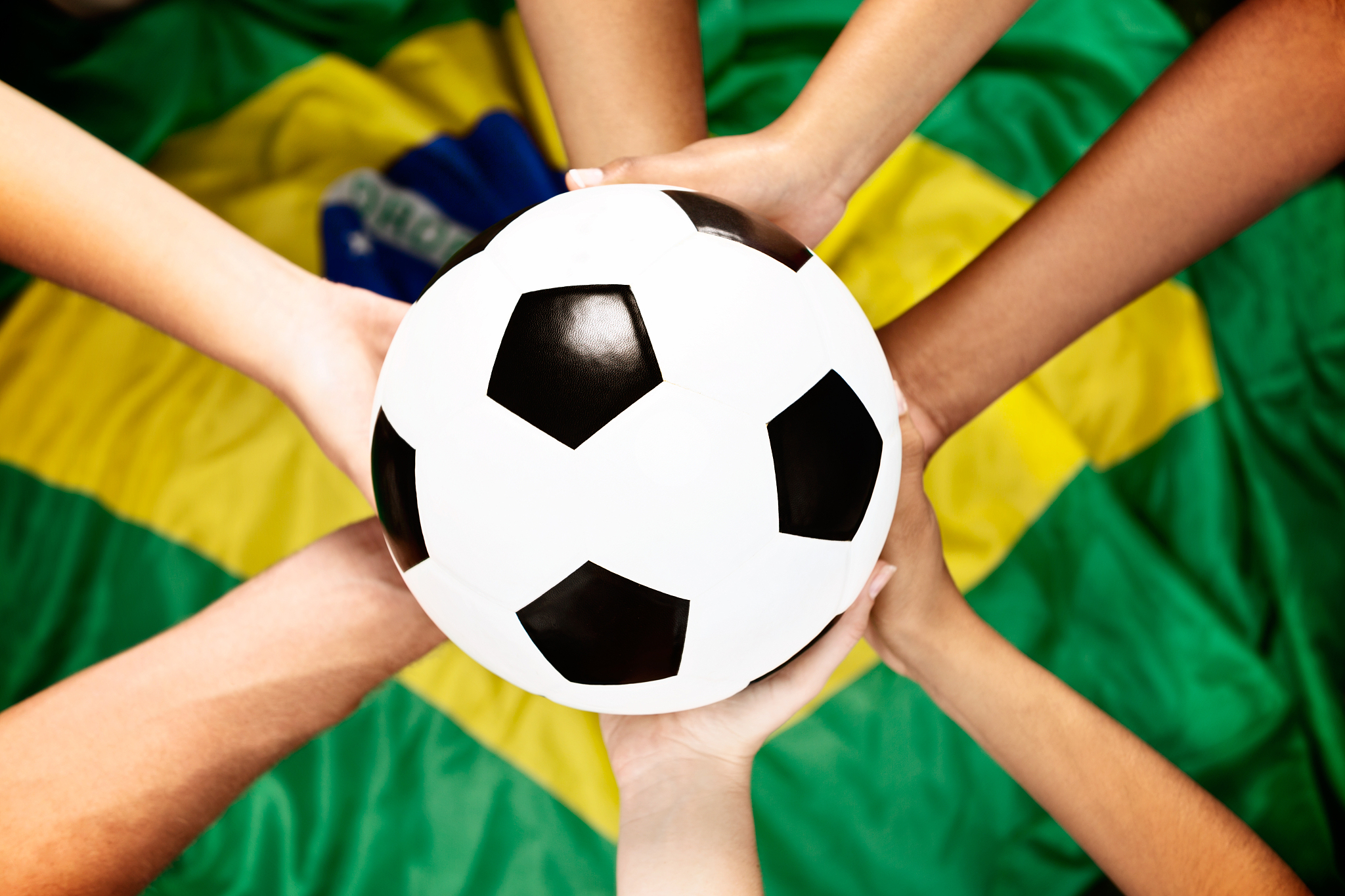 seven hands hold soccer ball against brazilian flag