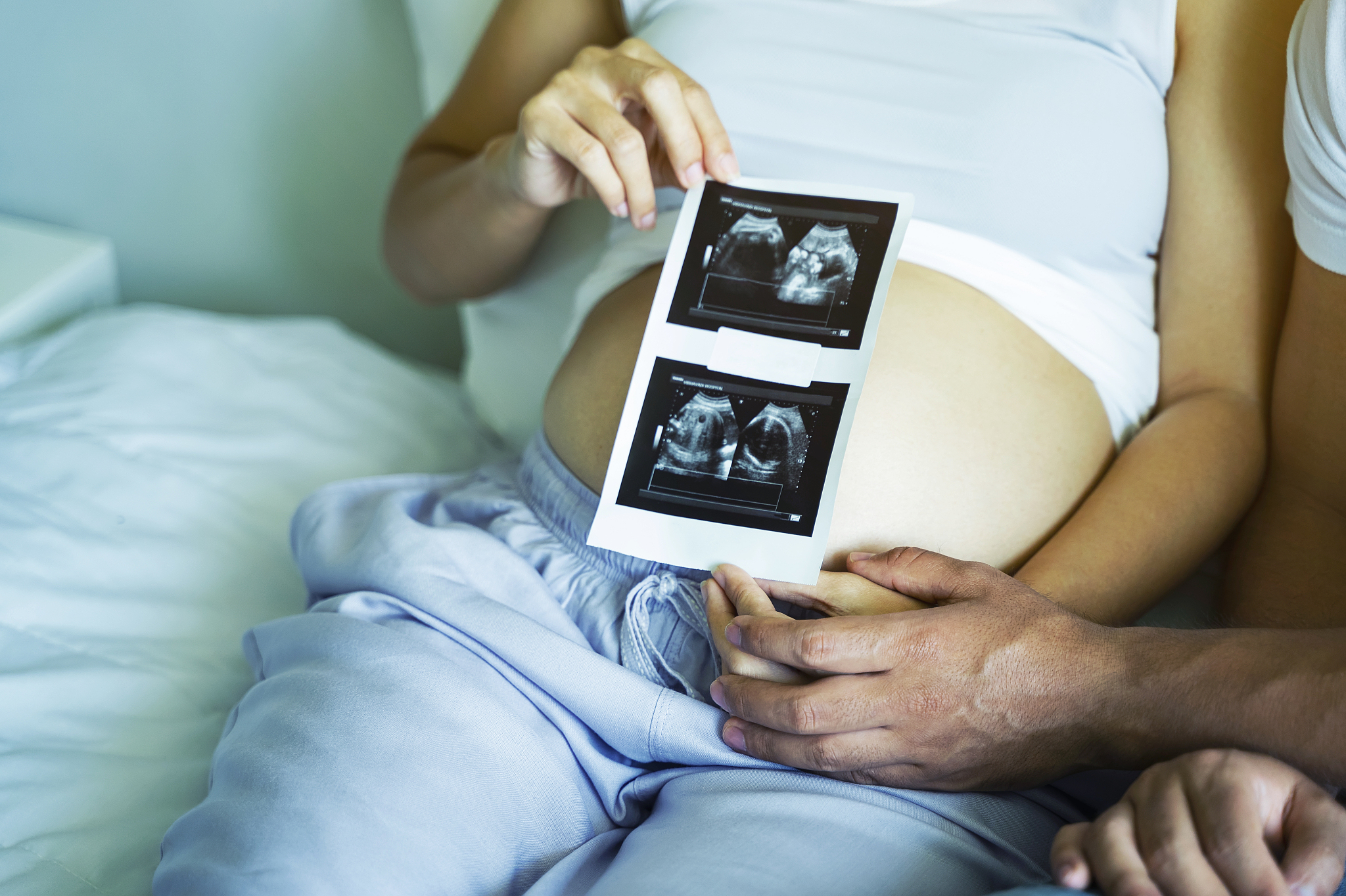 closeup of pregnant woman with ultrasound film of her baby on be
