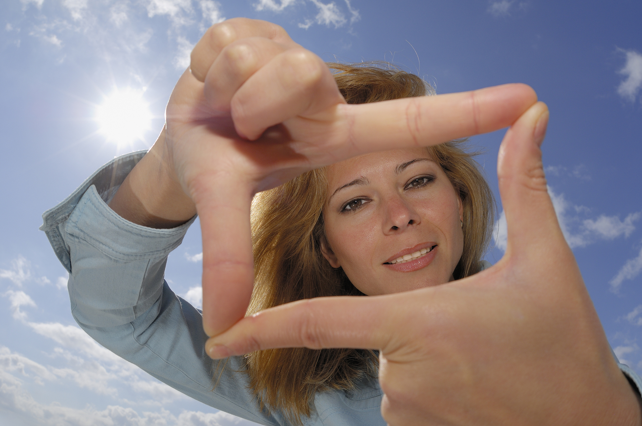 young woman against sky with sun, forming finger frame, portrait