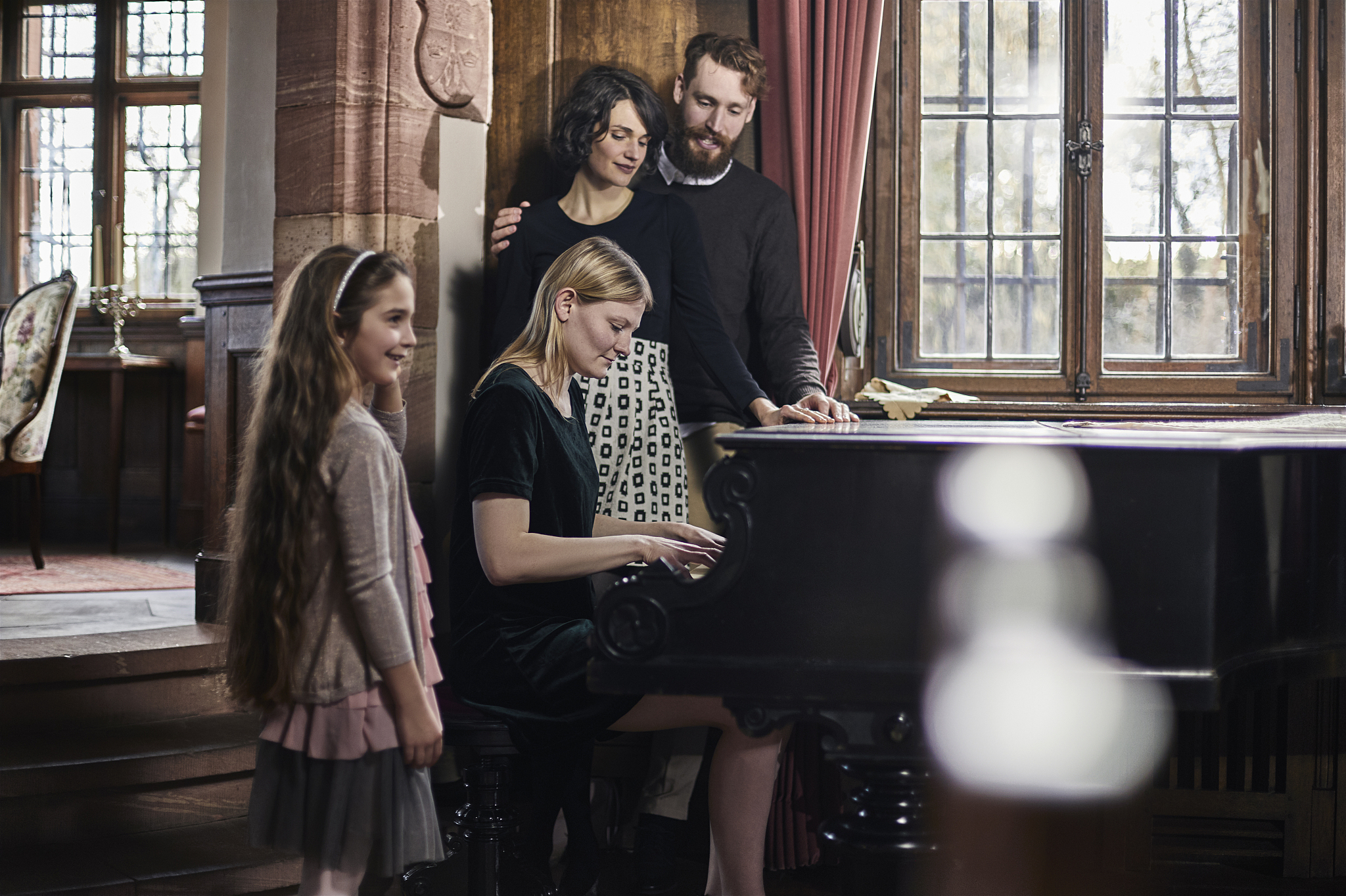 young woman playing piano watched by her family