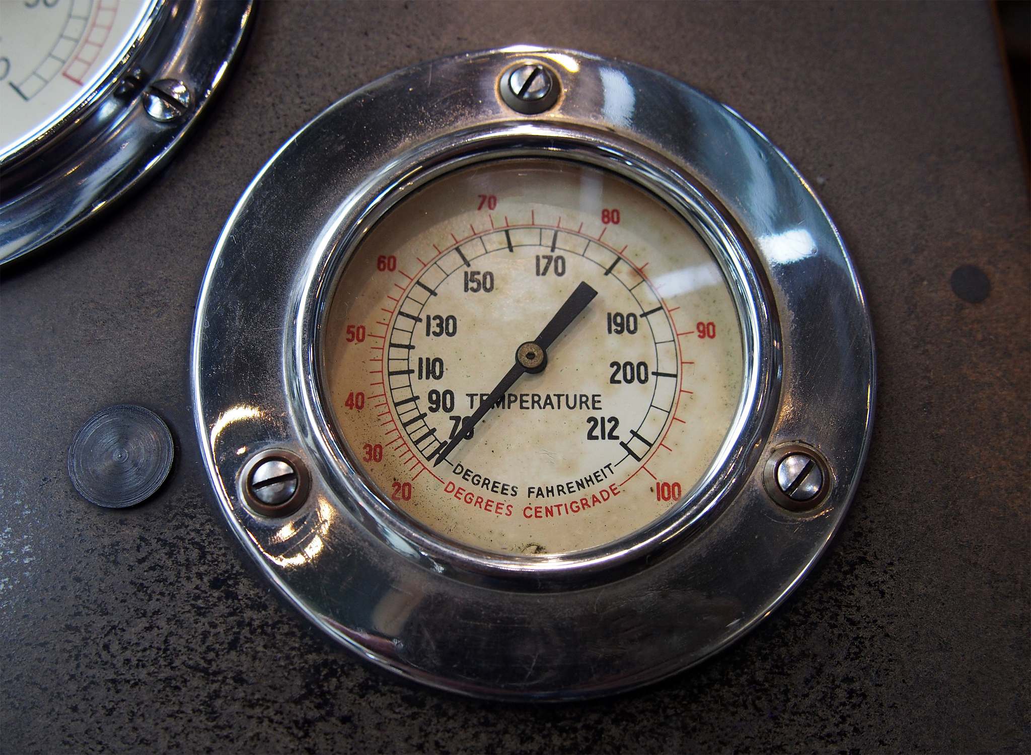 close up of an old round metal temperature gauge with the meter 