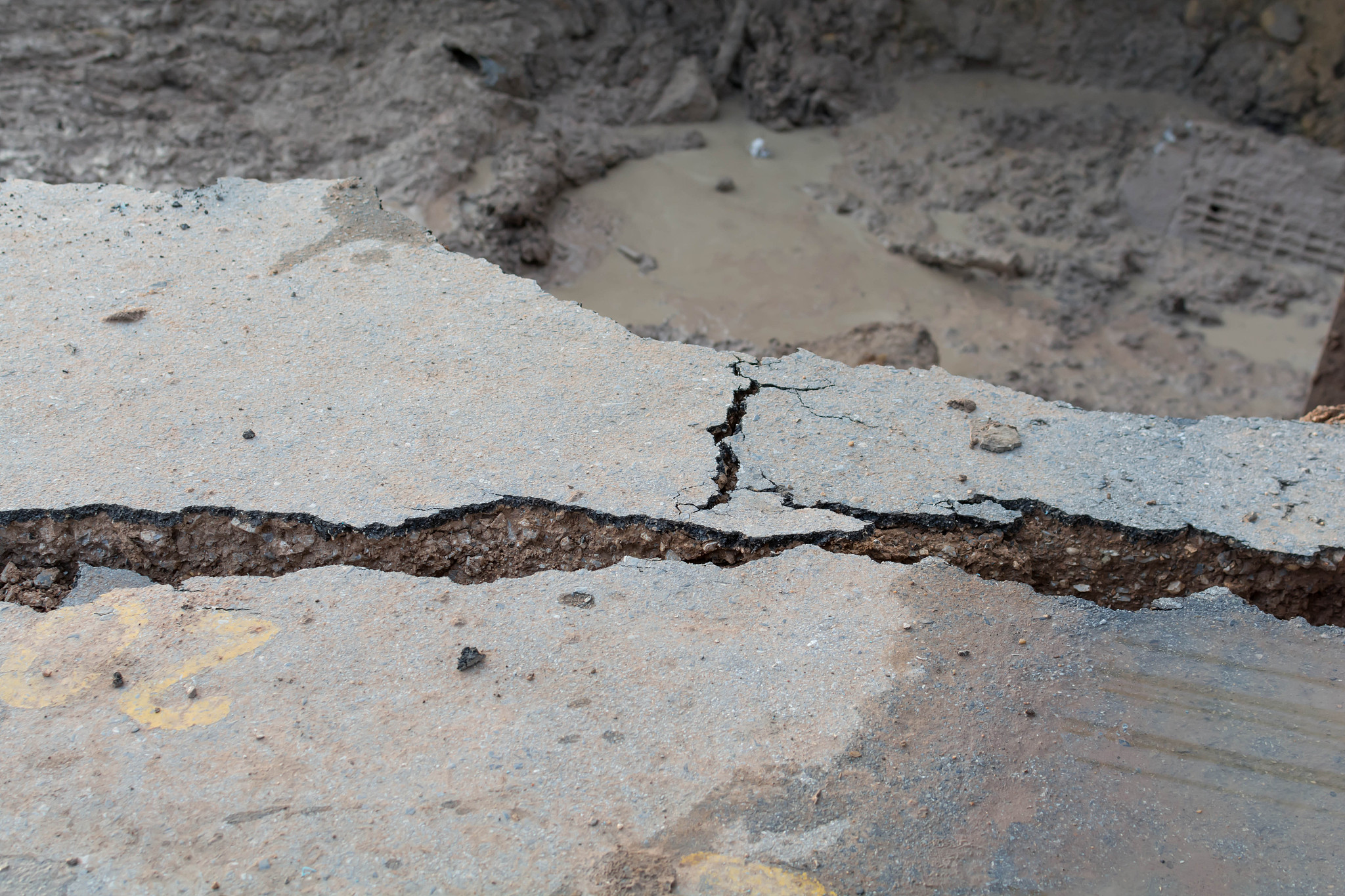 总结这一段话然后改写。盐碱土对路基造成危害，会导致路面不均匀沉陷，呈波浪形的鼓包，同时还会产生纵向裂缝和坑槽。每到季节性翻浆，路基含水量增大，地面会呈现弹簧状态并冒泥浆，这严重阻碍了交通运输业的发展。此外，盐碱土中的硫酸会随风迁移，若附着到混凝土建筑物表面，雨雪水溶解后会浸入建筑物表面的细小缝隙中，形成含大量结晶水的硫酸盐。字数不能少于原文