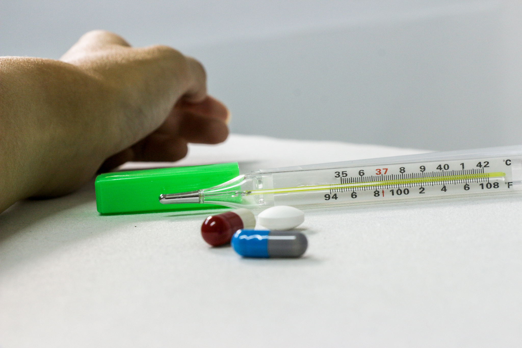 patient hand with various pills and thermometer