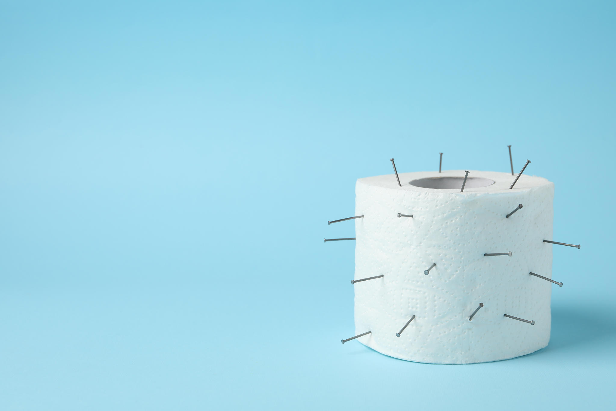 toilet paper with nails on blue background, space for text