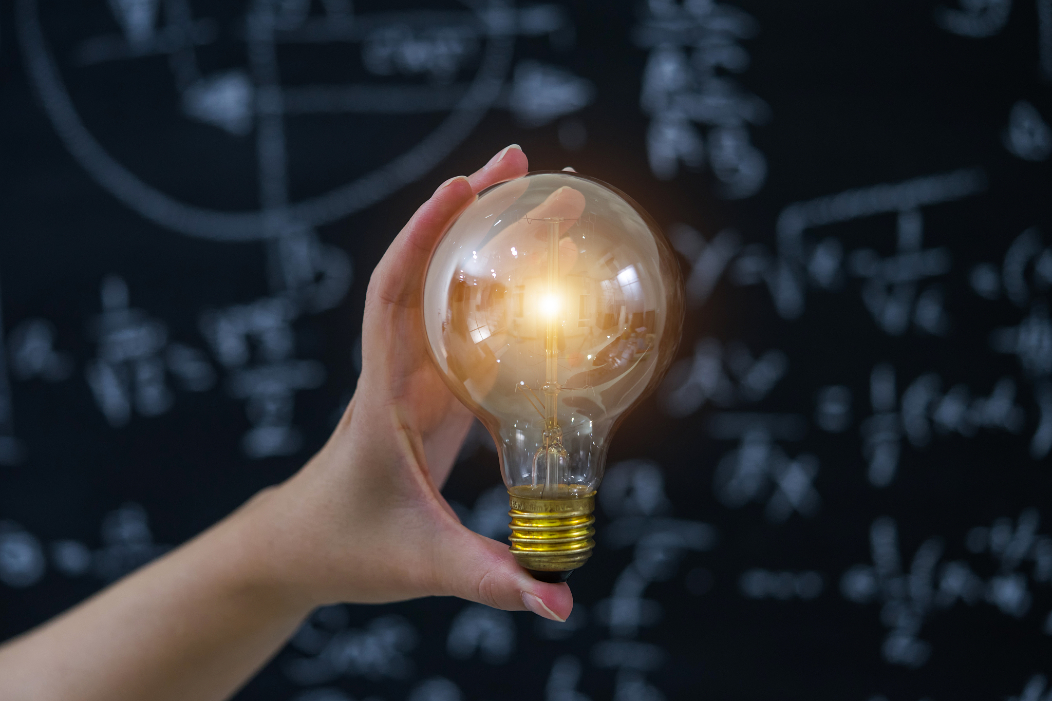 hand holding light bulb on blackboard background.