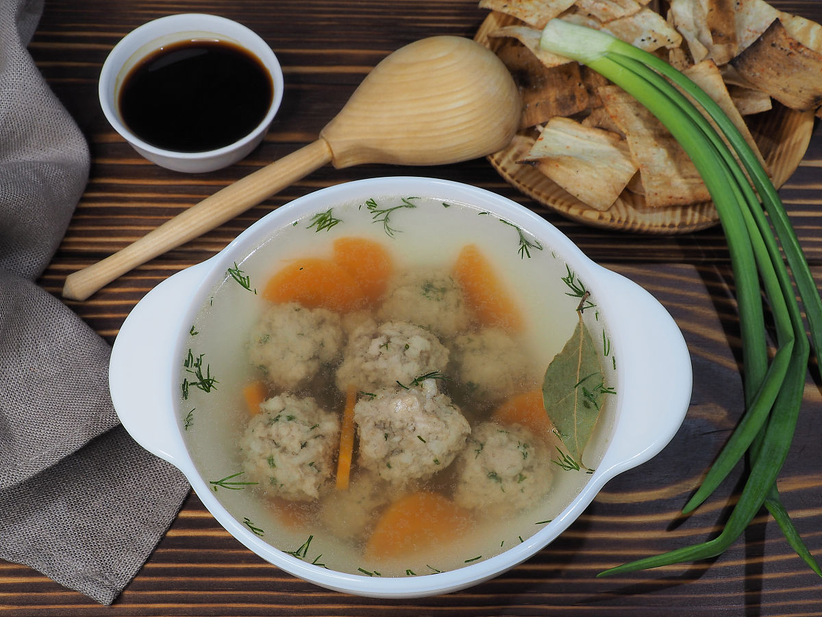 白色碗里的热肉丸汤配胡萝卜和香草,木桌上的酱油,俯视图,平面布局.透