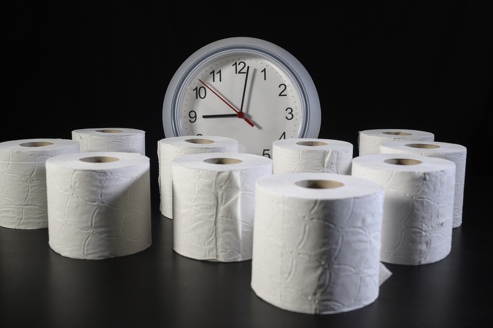 a table appears full of full rolls of toilet paper with a clock 