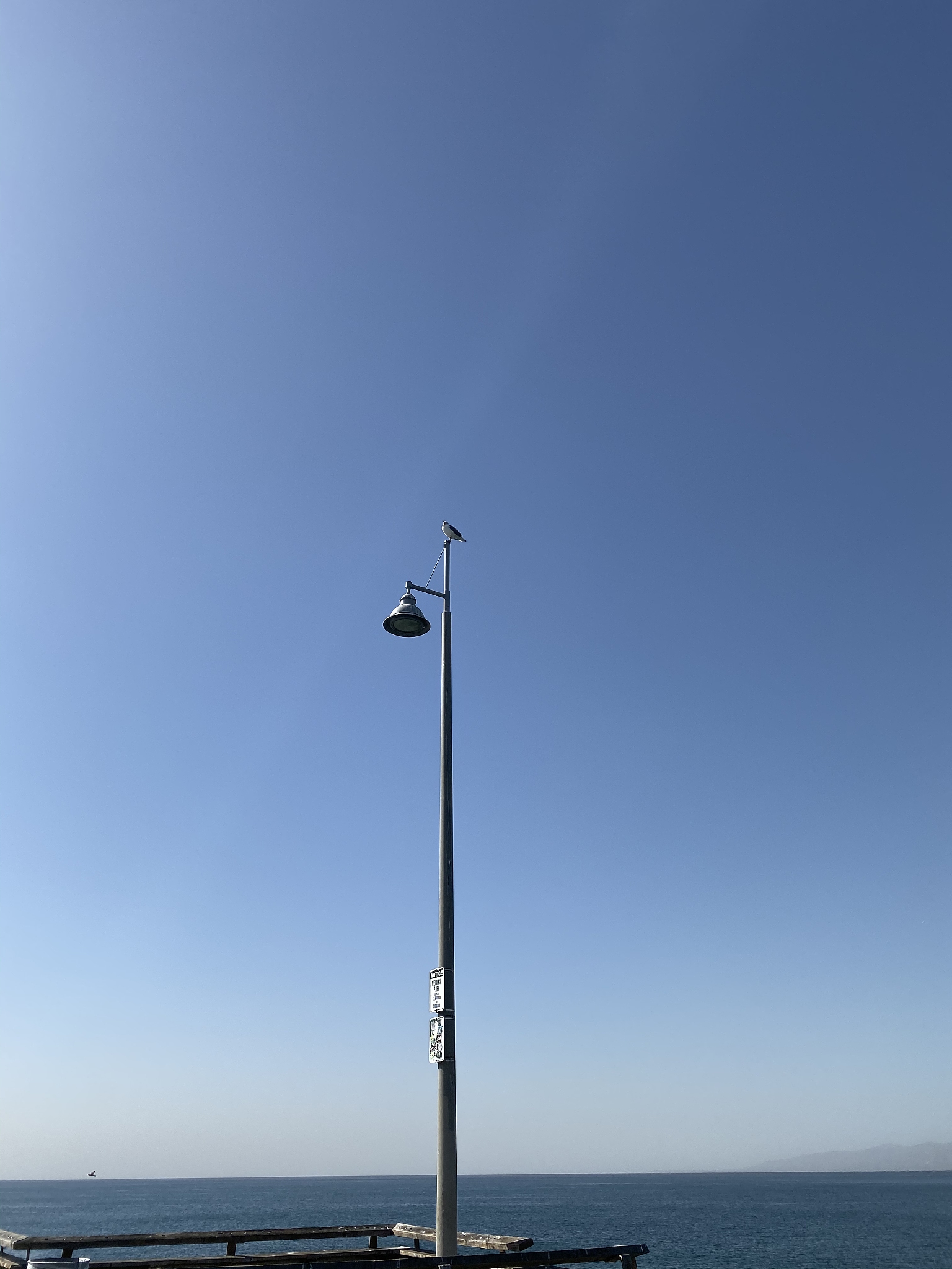 street light by sea against clear blue sky