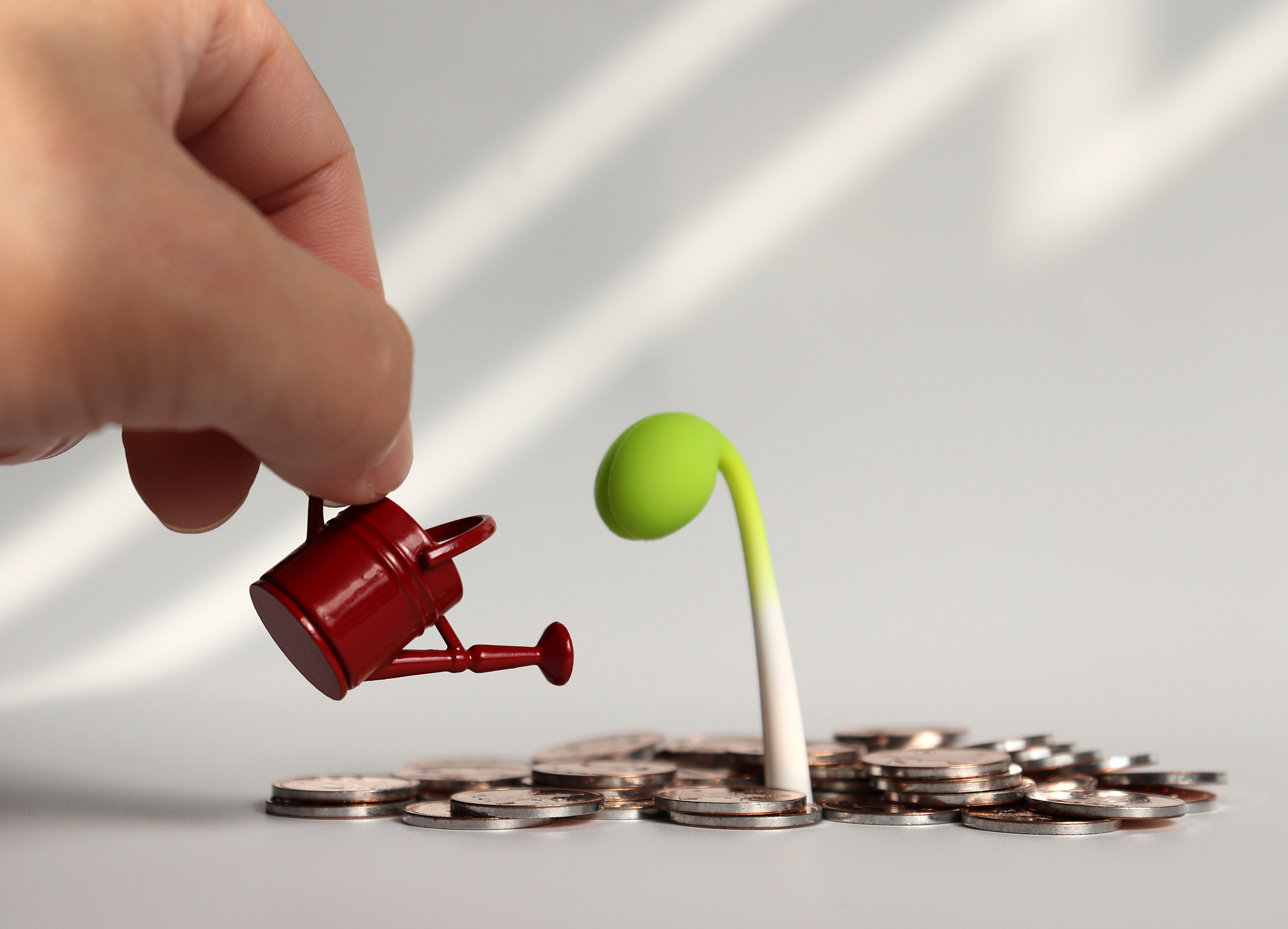 a hand holding a watering can and coins.