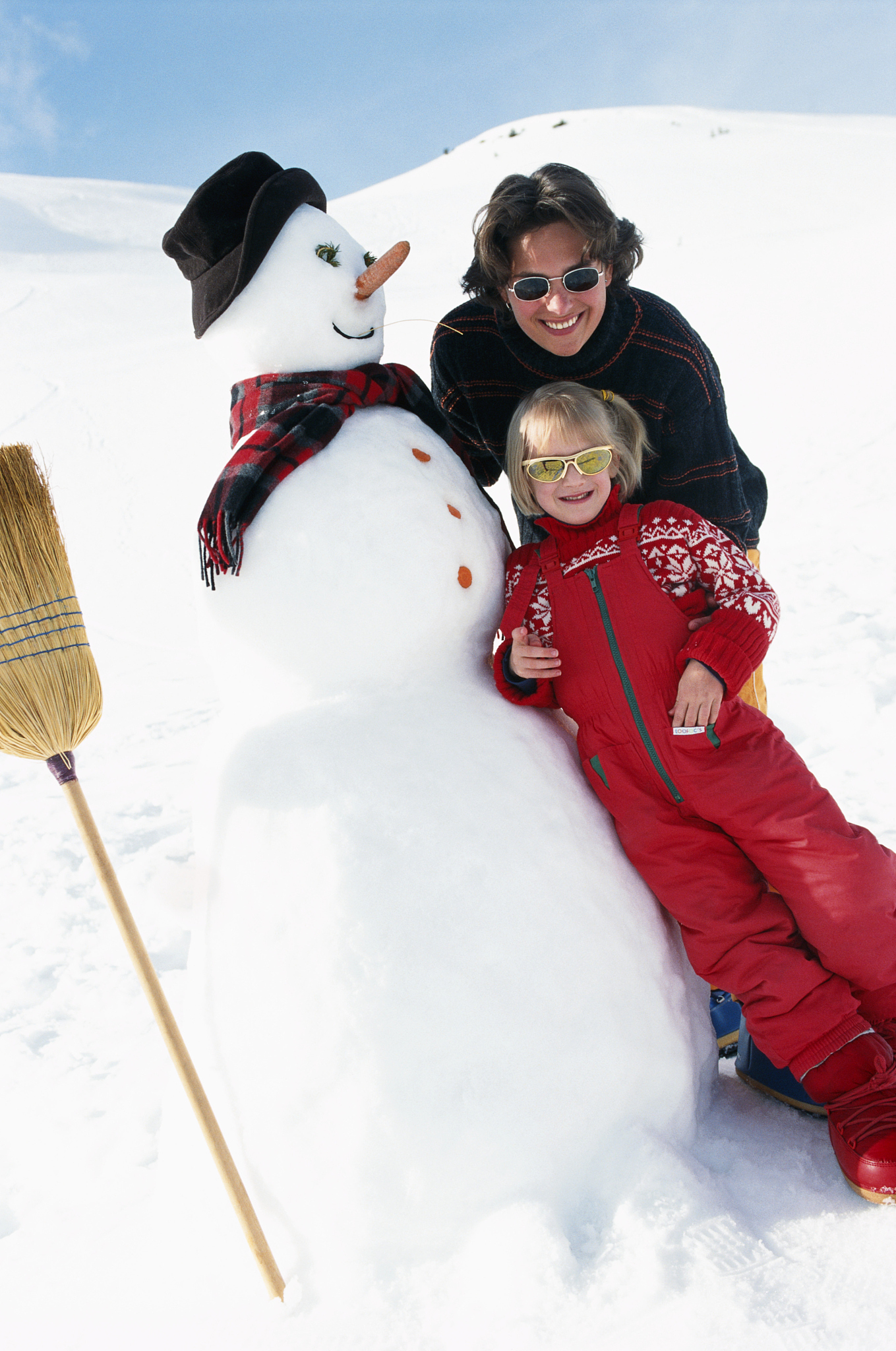 mother and daughter standing with snowman