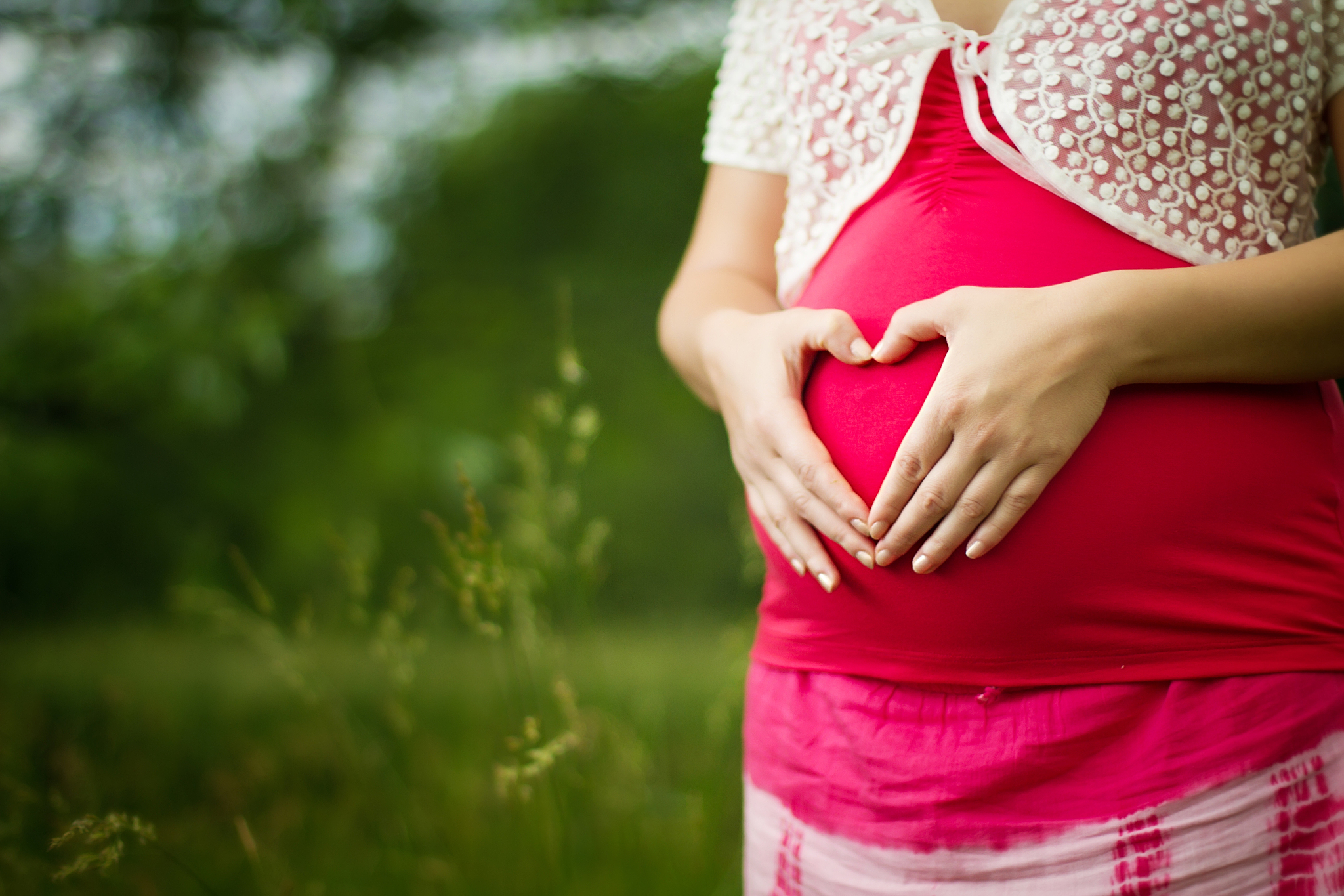 young pregnant woman caressing her belly, making heart shape