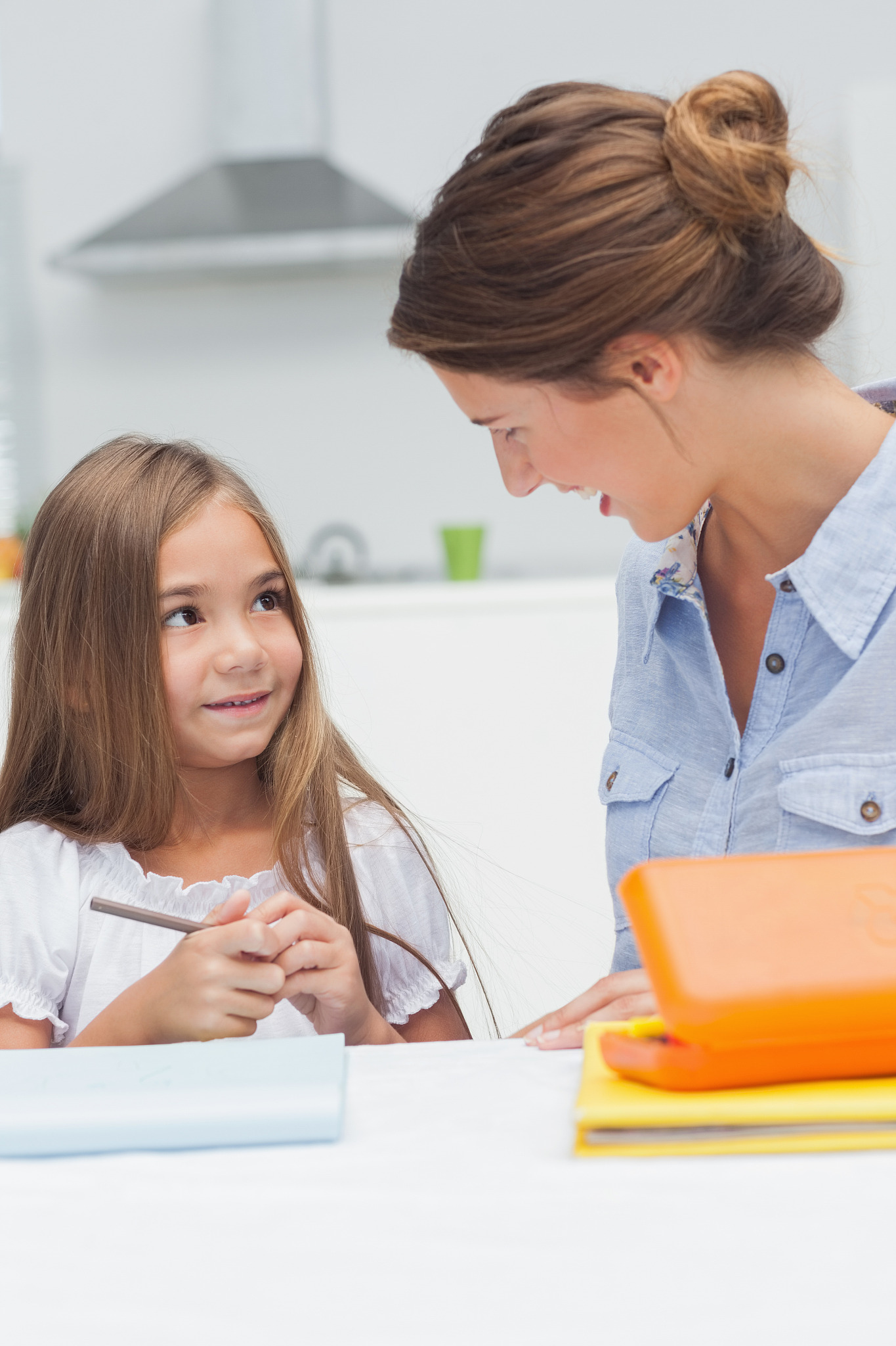 mother chatting with her daughter drawing in the kitchen