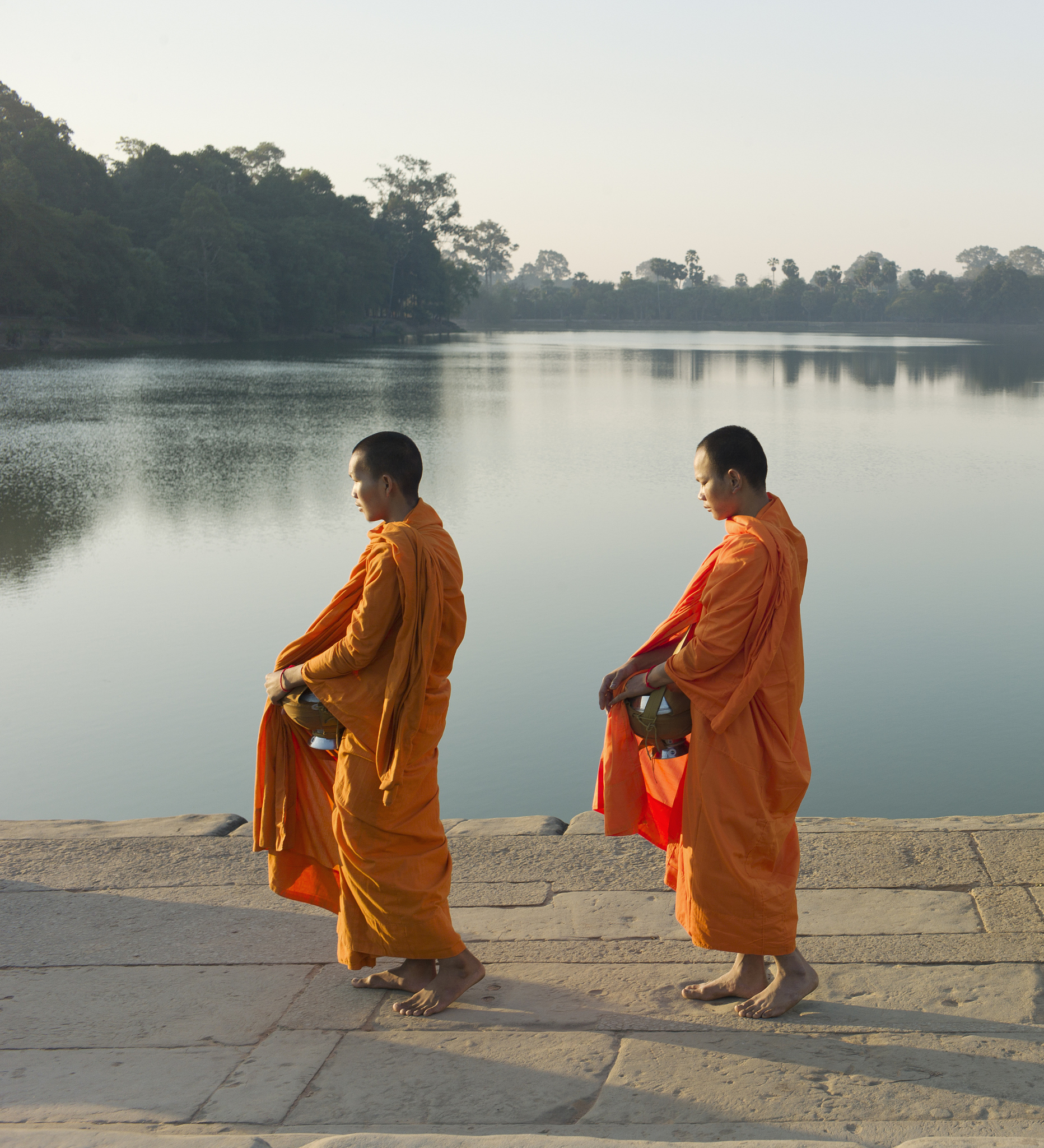 buddhist monks walking in front of water edge