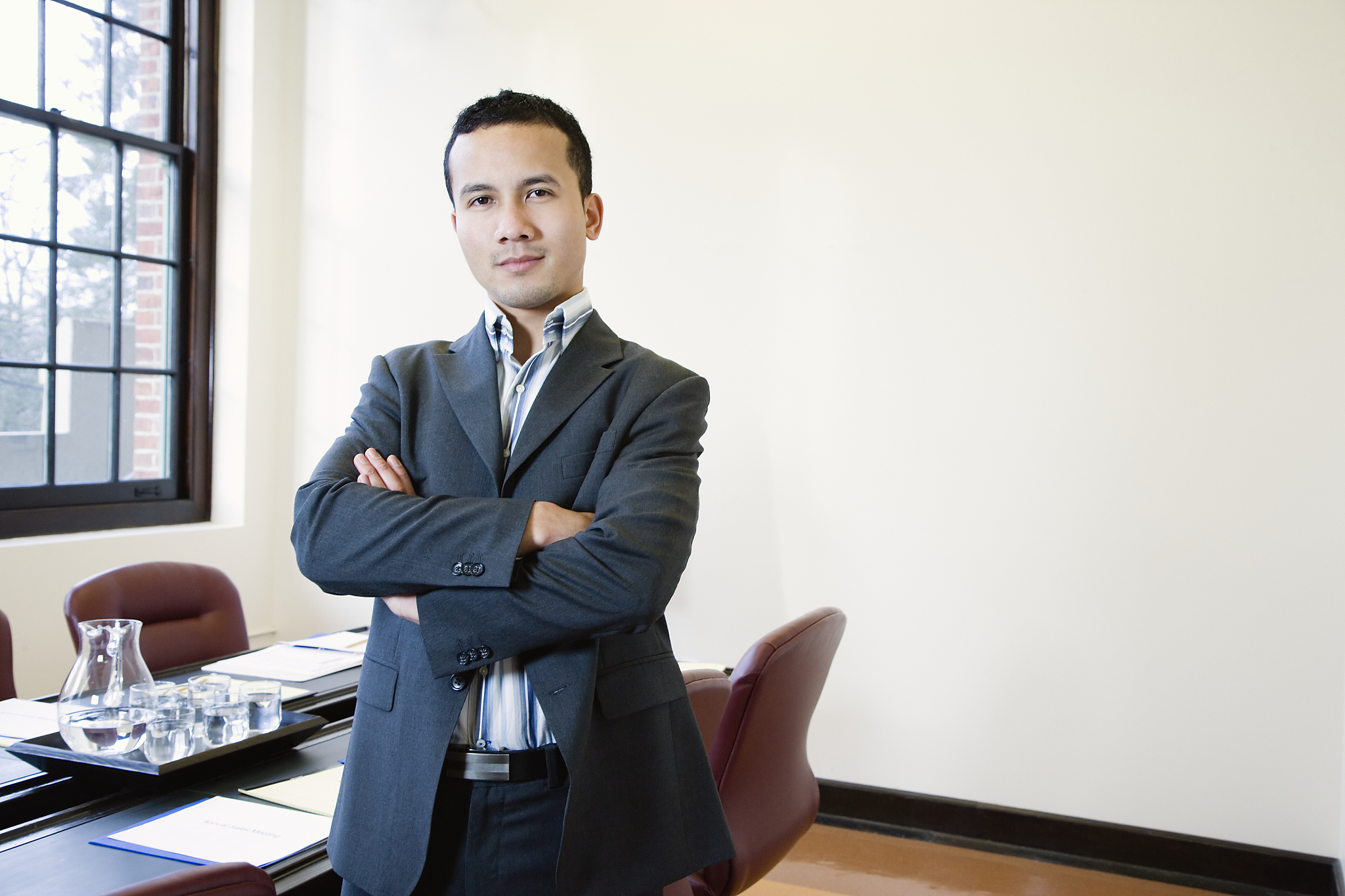 young businessman standing in boardroom, arms crossed, portrait