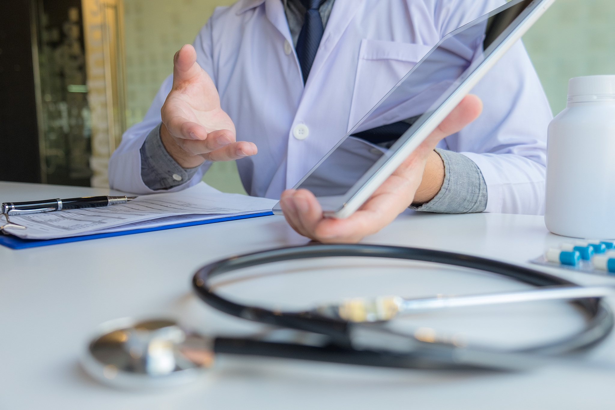 midsection of doctor showing digital tablet to patient at clinic