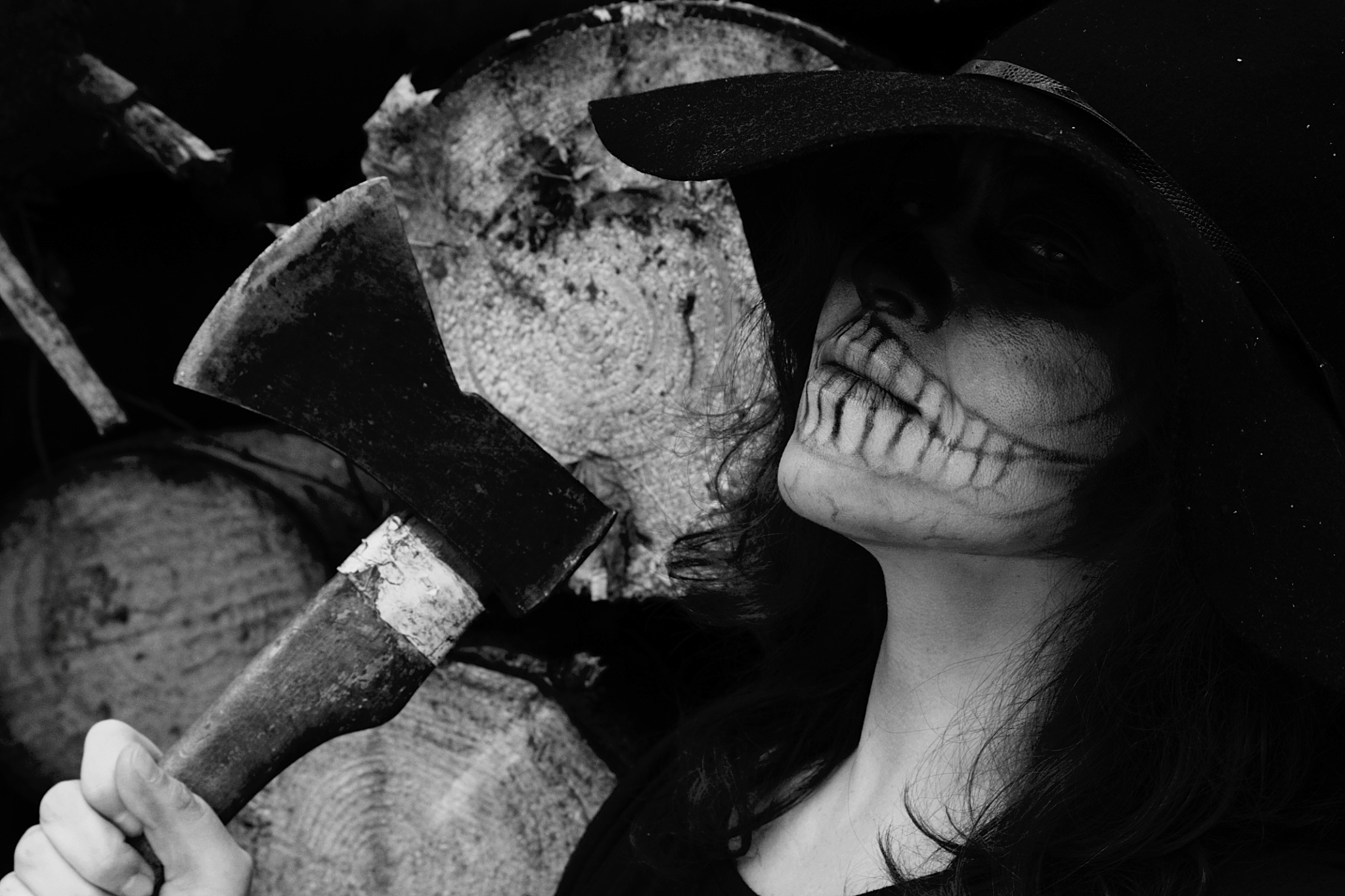 portrait of woman with zombie costume holding axe by wooden logs