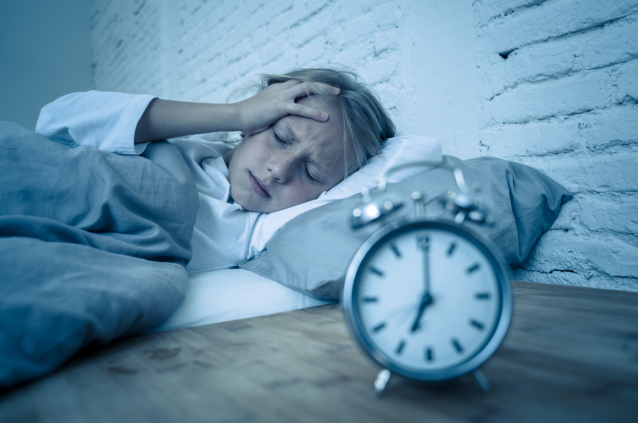 sweet sleepless little girl lying sad in bed looking at alarm cl