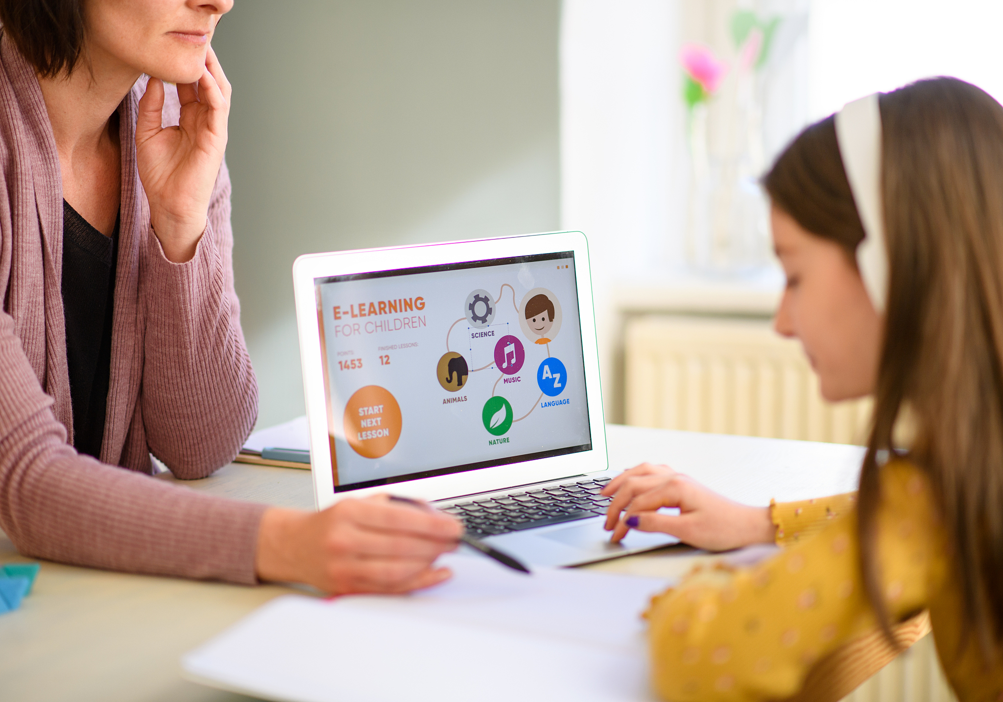 small schoolgirl with mother sitting at the desk indoors at home