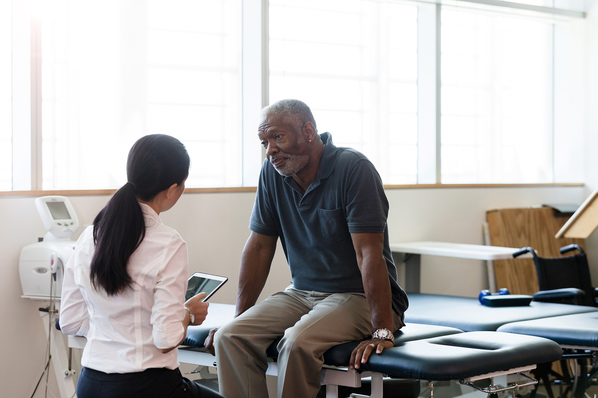physical therapist reviews treatment while mature man listens