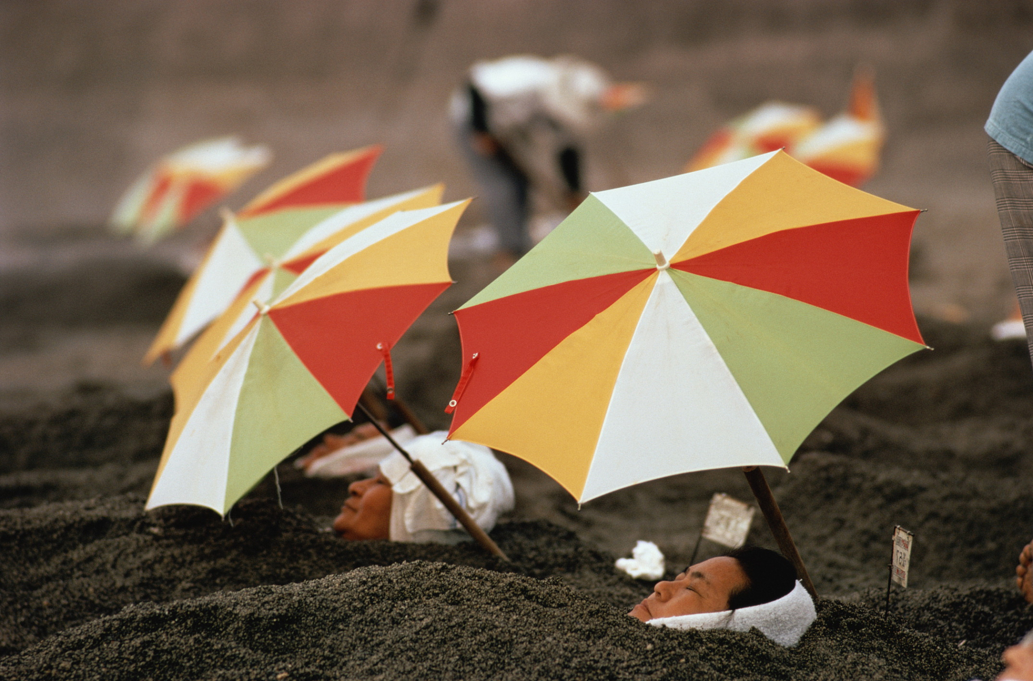 japan,kyushu,women soaking in hot thermal sands under umbrellas