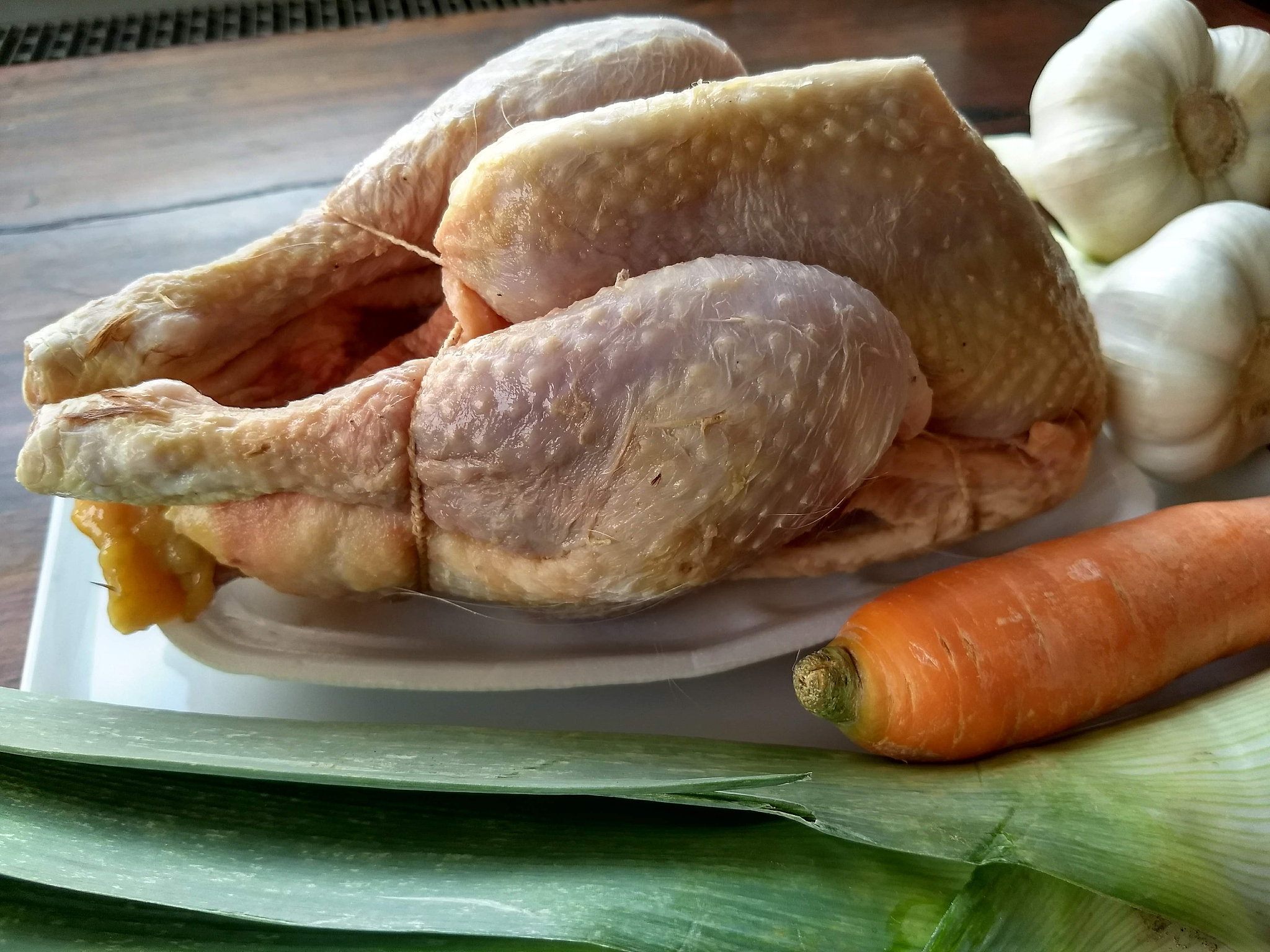 ein rohes suppenhuhn mit suppengrün und knoblauch drum herum dr