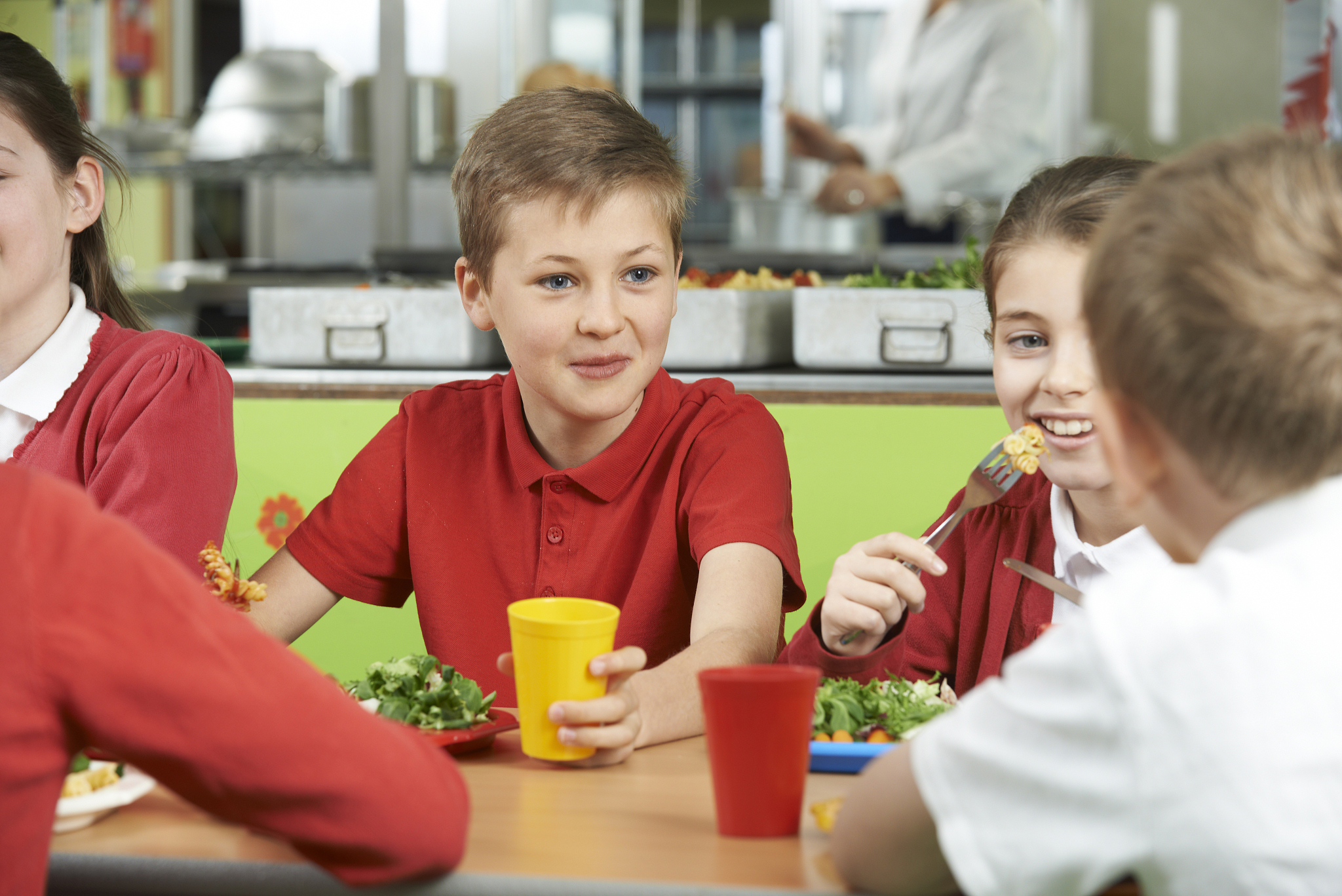 group of pupils sitting at table in school cafeteria eating meal