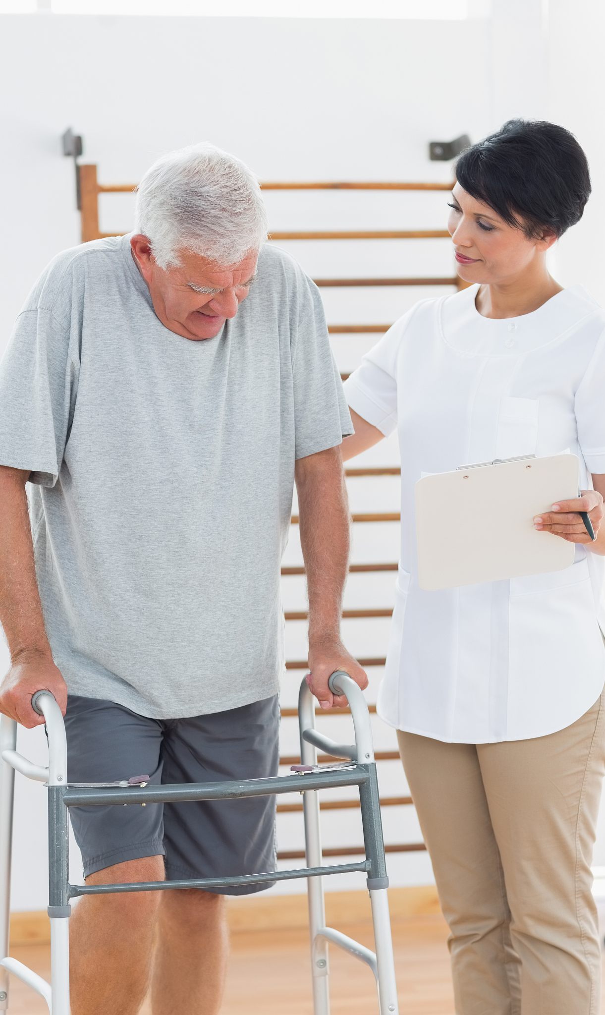 physiotherapist helping senior man to walk in gym