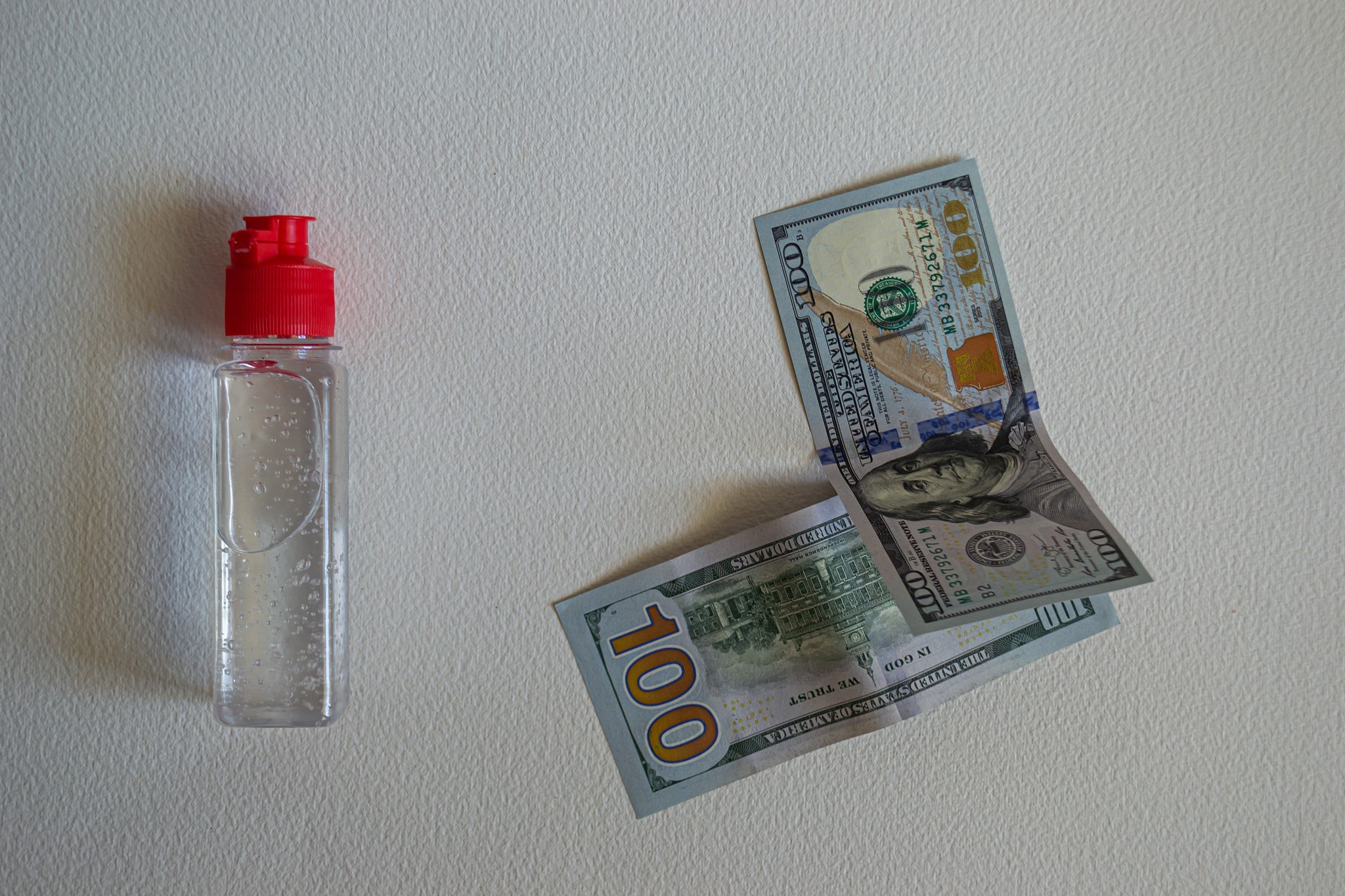 bottle of hand sanitizer with two one hundred-dollar bills on wh