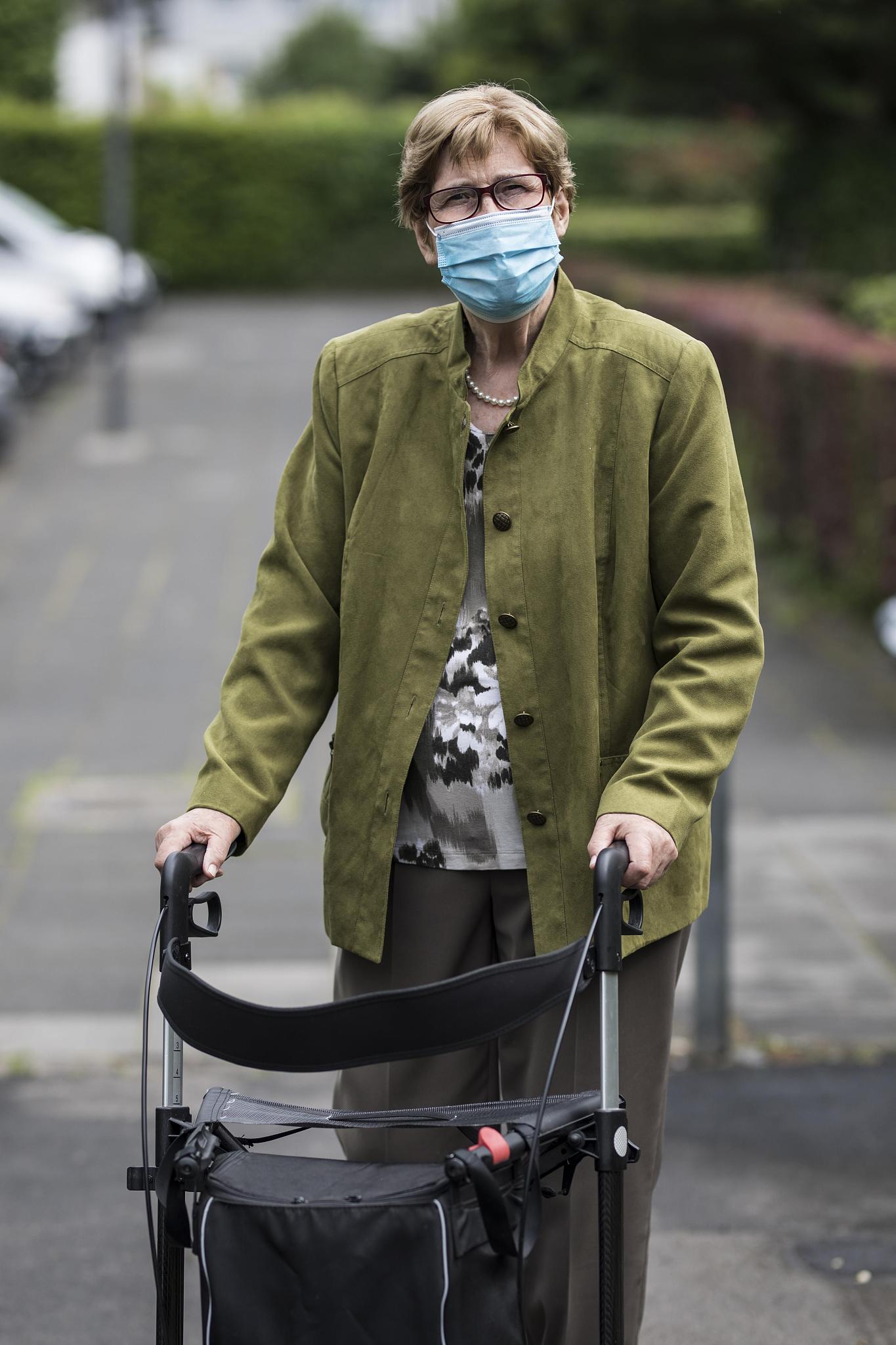 senior citizen with mouth and nose protection and rollator on th