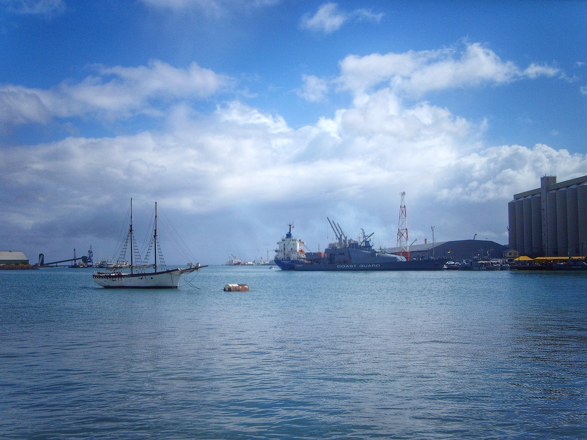 sailboat sailing on sea by commercial dock against cloudy sky