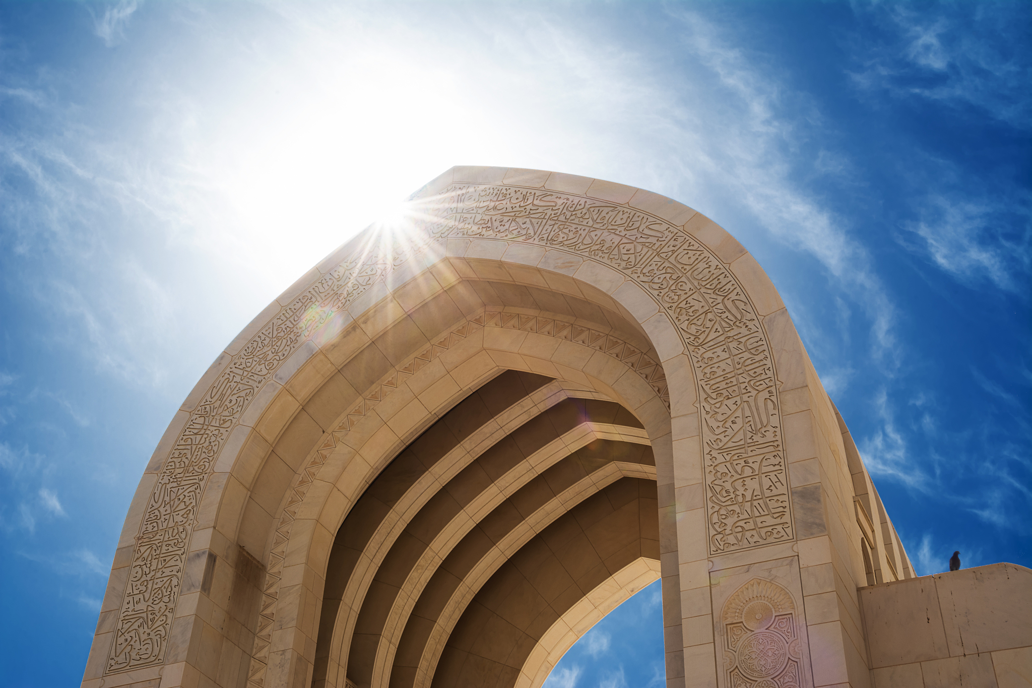 detail of an arch of the muscat grand mosque with sun in backlig