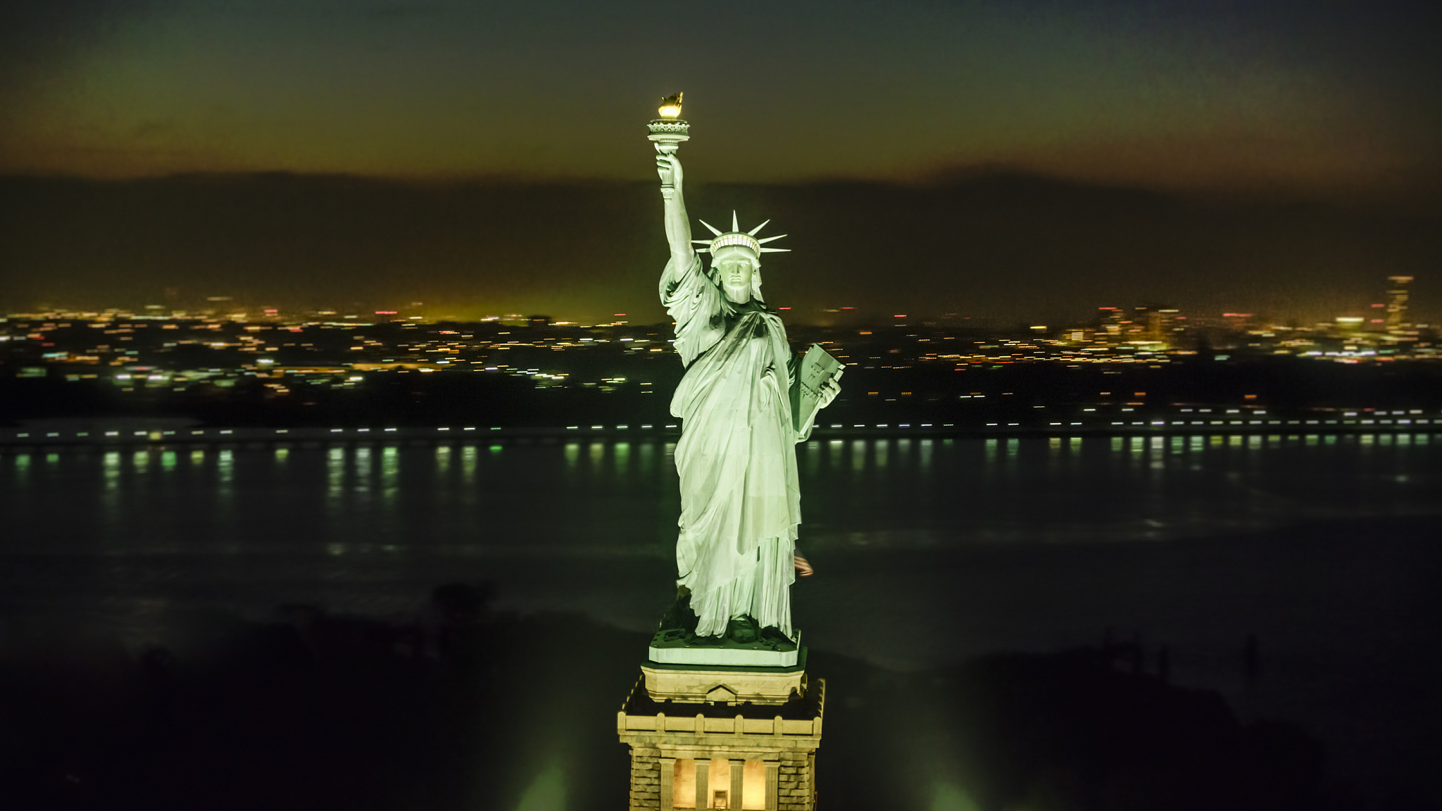 statue of liberty shining in the night with lower manhattan seen