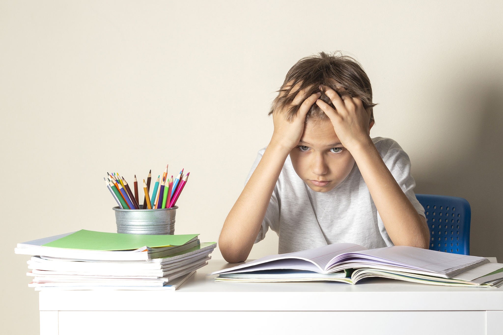 tired upset schoolboy with pile of school books and notebooks