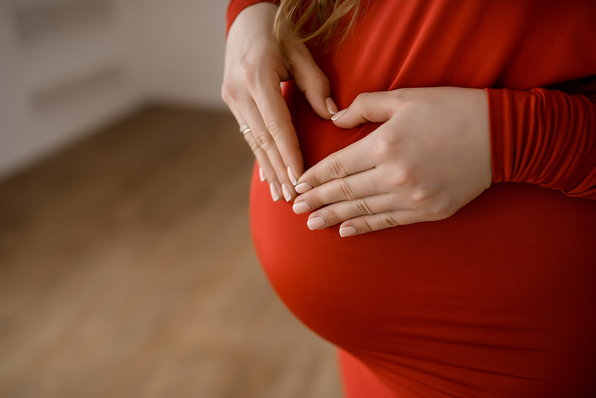a pregnant woman in a red dress holds her pregnant belly with he