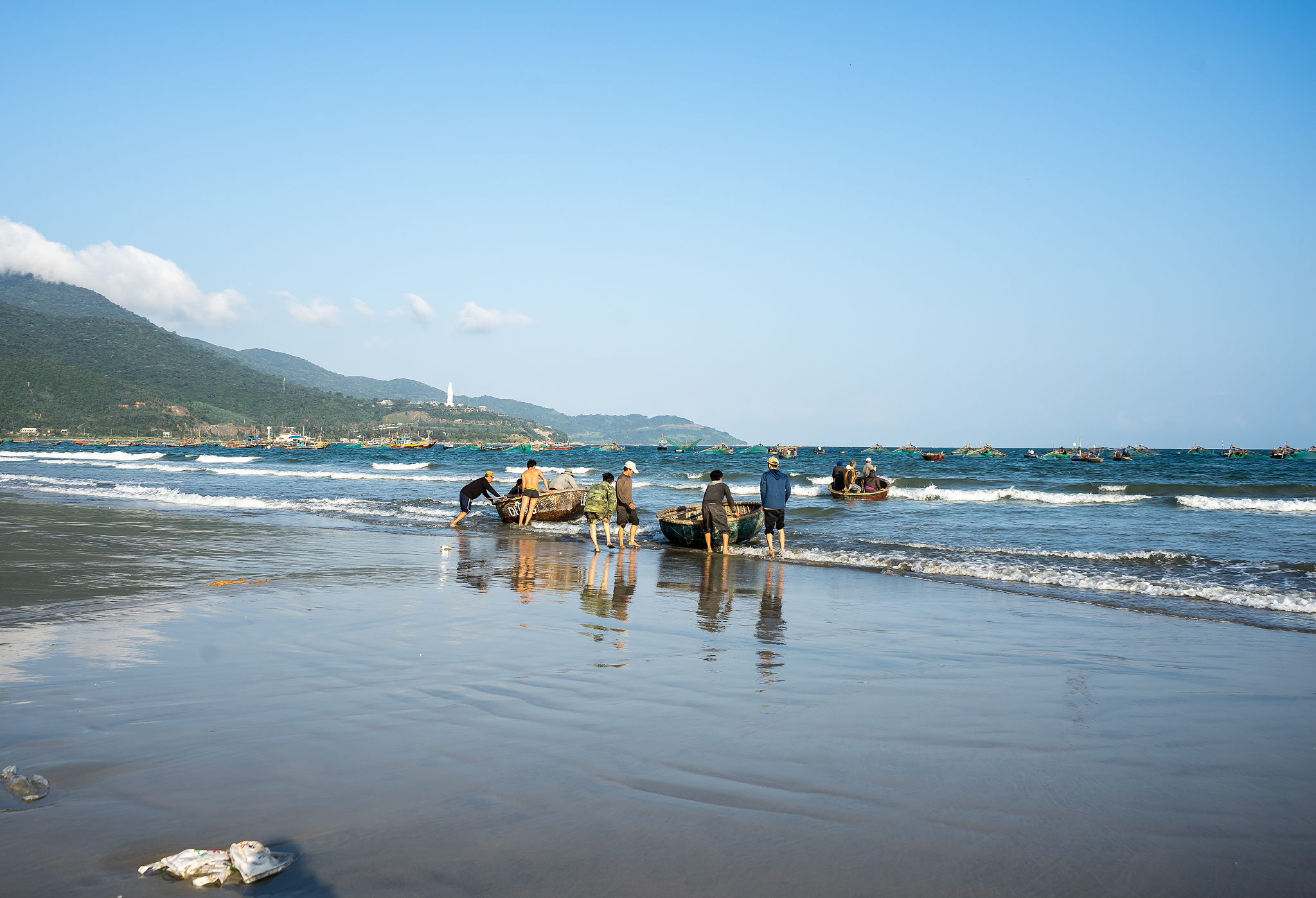 people pushing fishing boats at sea shore