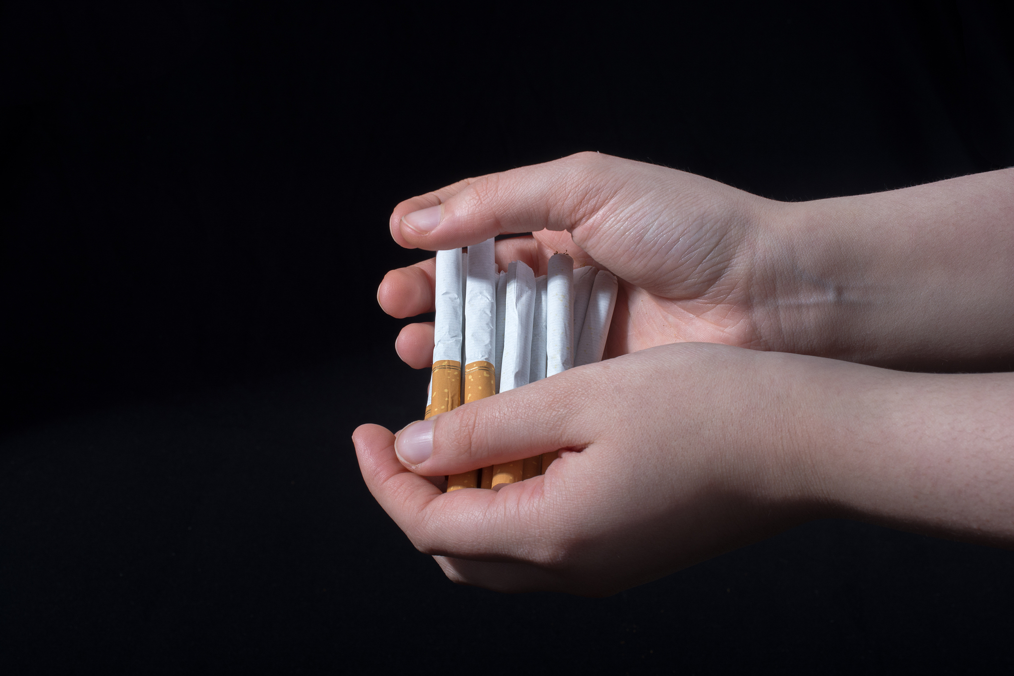 cropped hands holding cigarettes over black background