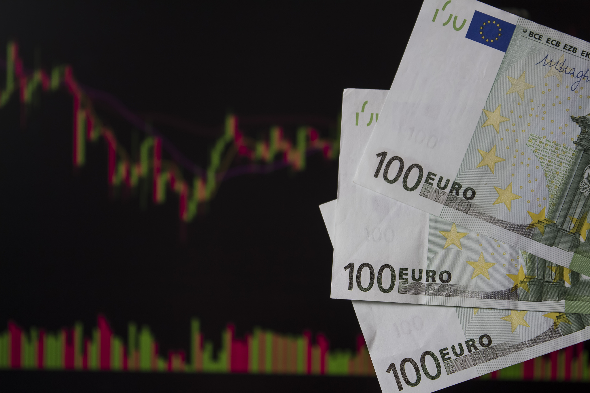 hands holding euro, eur in front of a laptop monitor with a pric