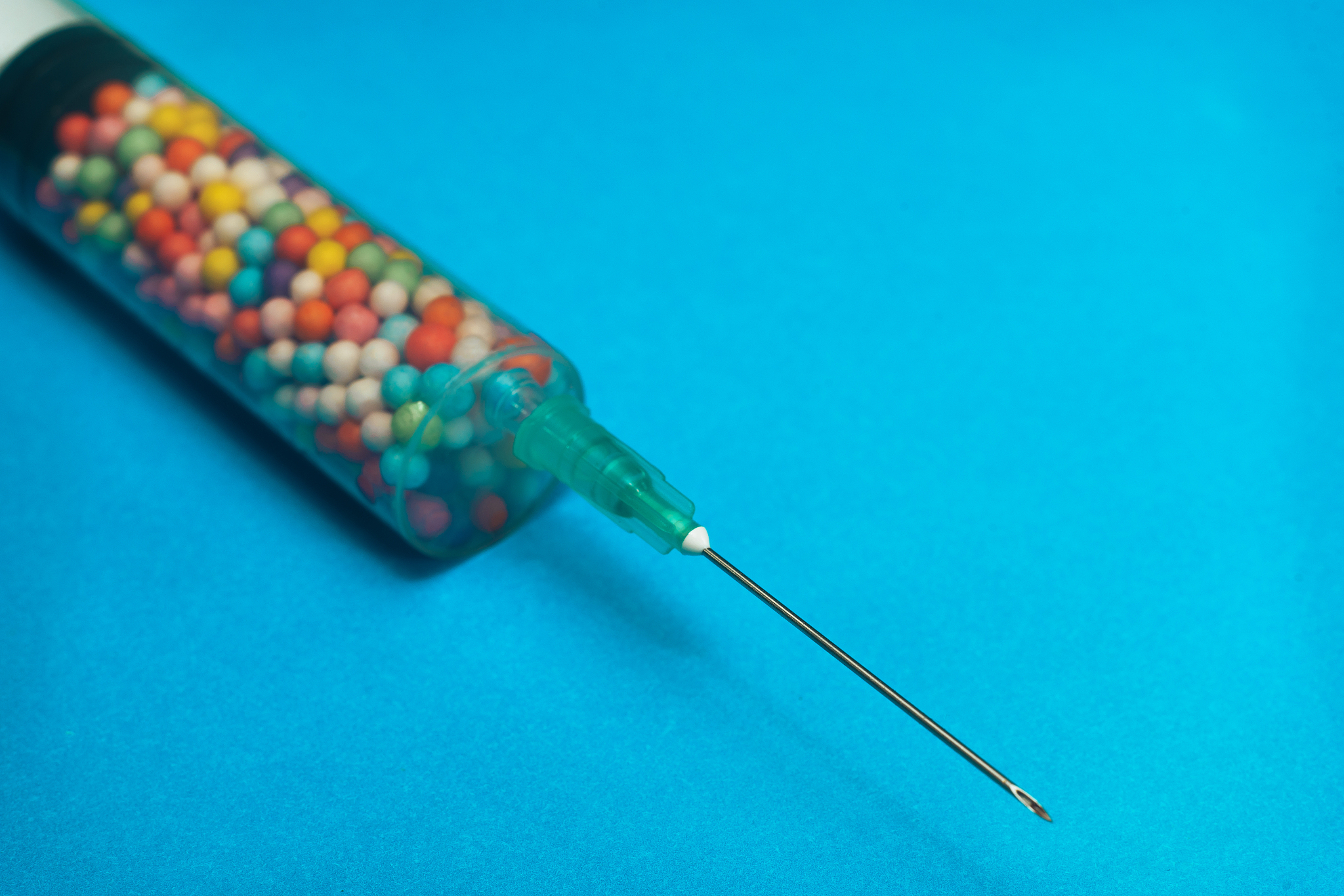 syringe filled with colorful nano balls on a blue background. in