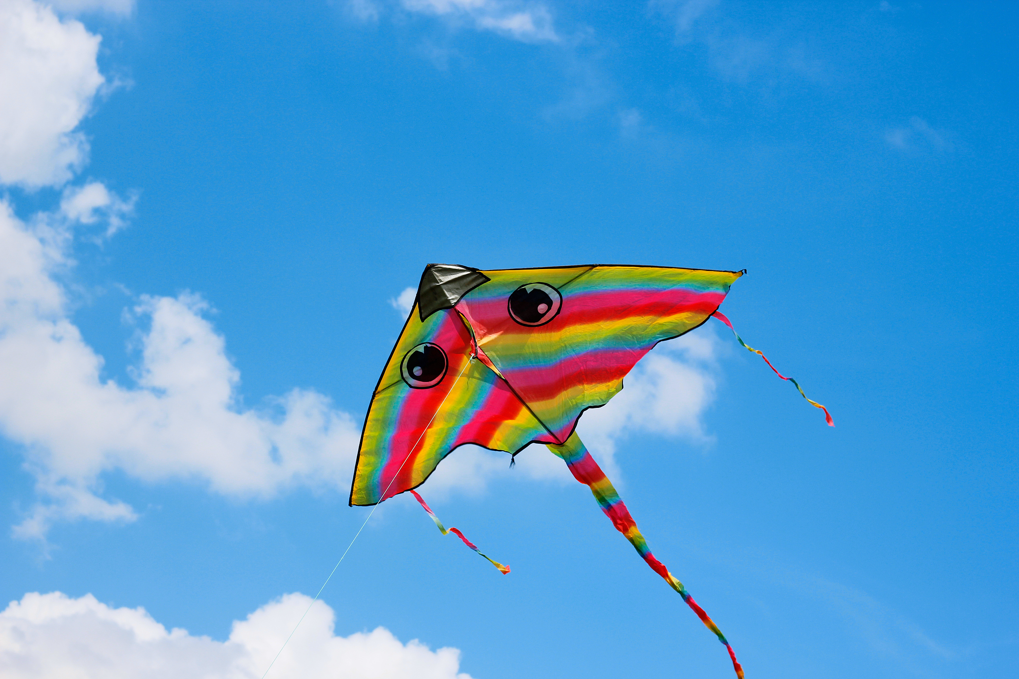bright kite flying in the clouds and blue sky in the background.
