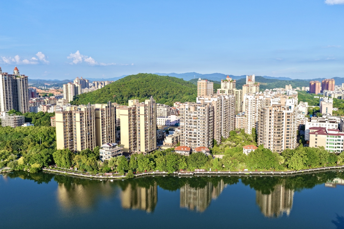 宁静湖泊环绕着绿植与山丘,湖中倒映着高楼林立的城市