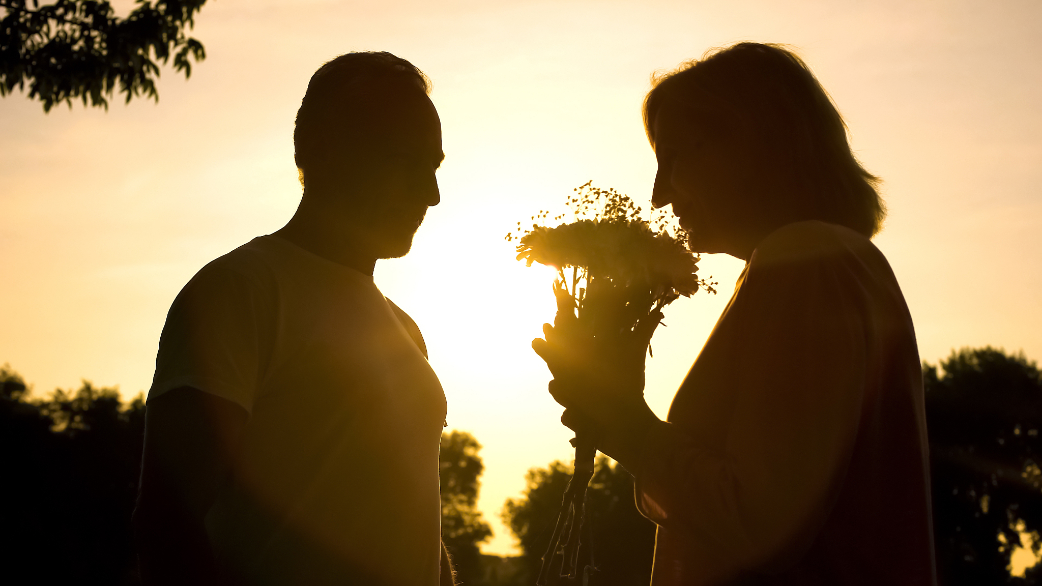 silhouette of woman smelling flowers presented by man, celebrati