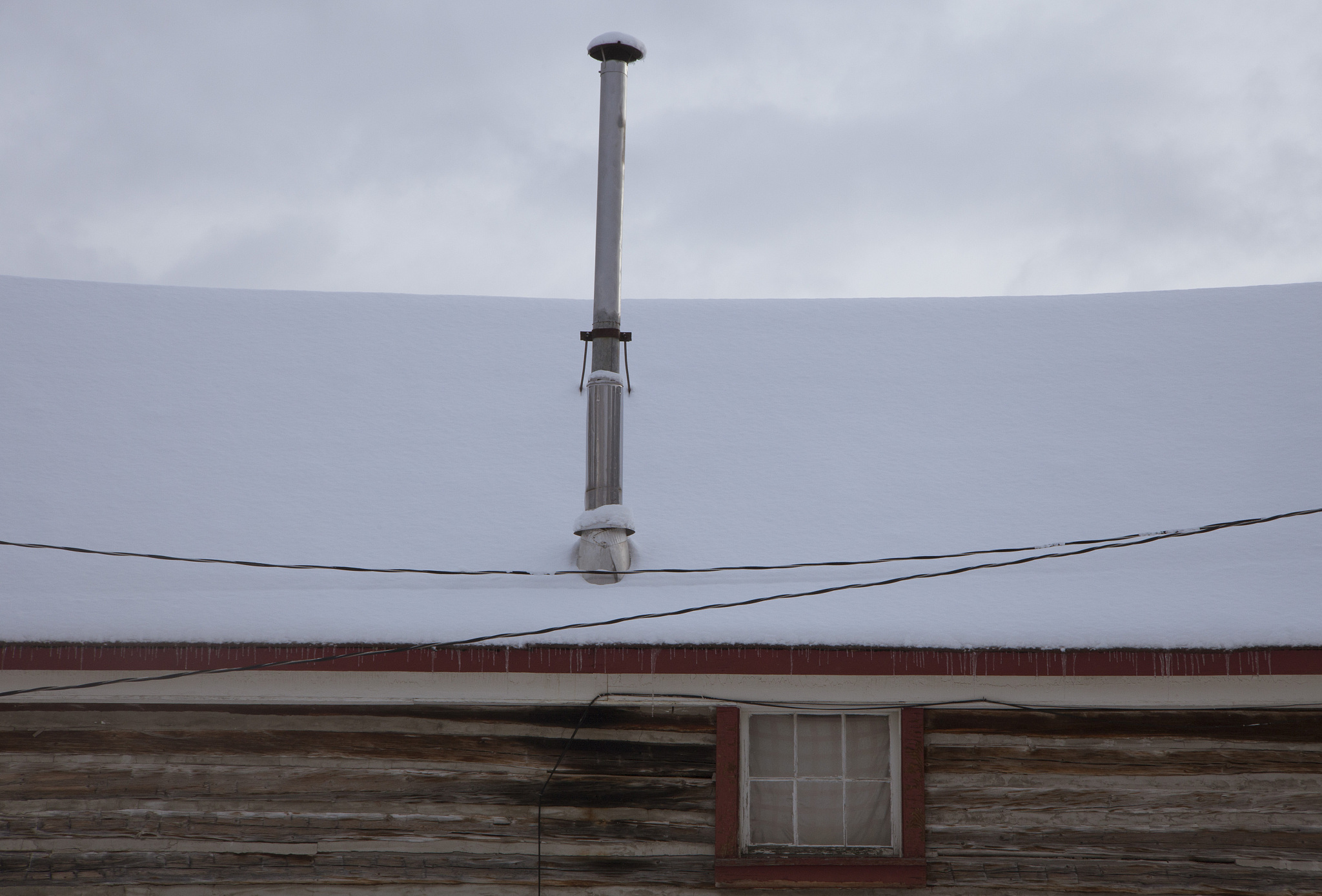 snowy log cabin rooftop with exhaust pipe