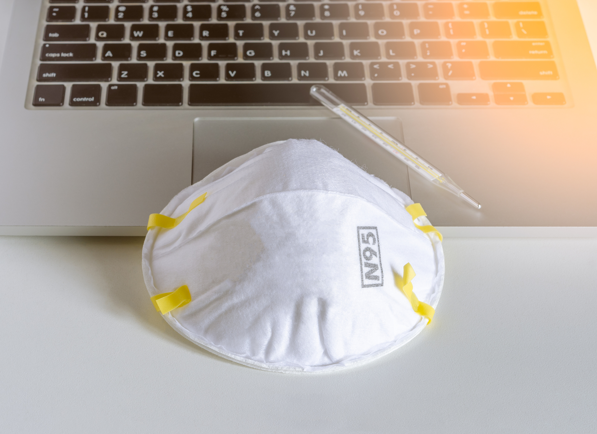 n95 respirator mask and mercury-in-glass  thermometer on laptop.