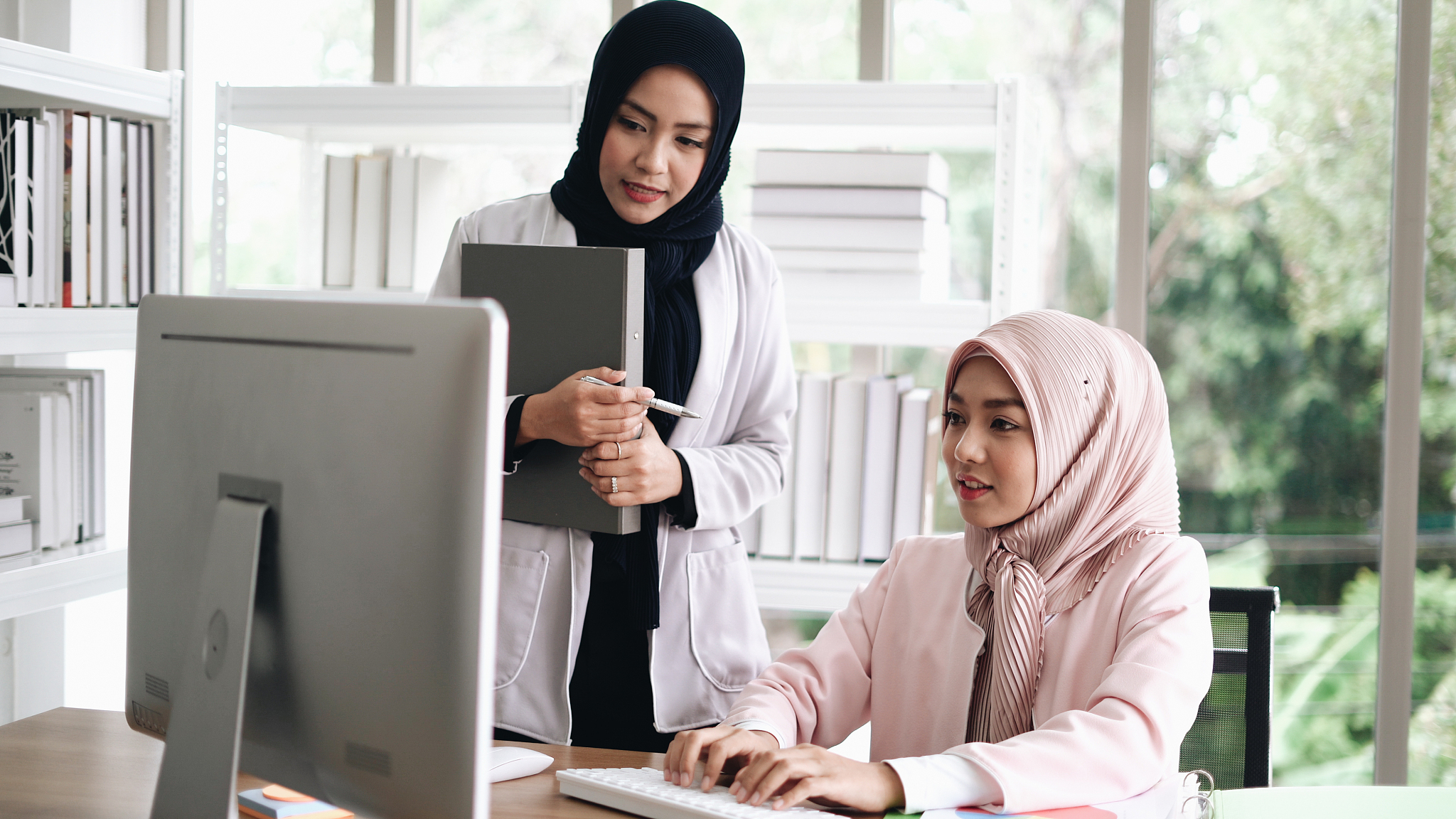 two woman with hijab working on laptop in office.