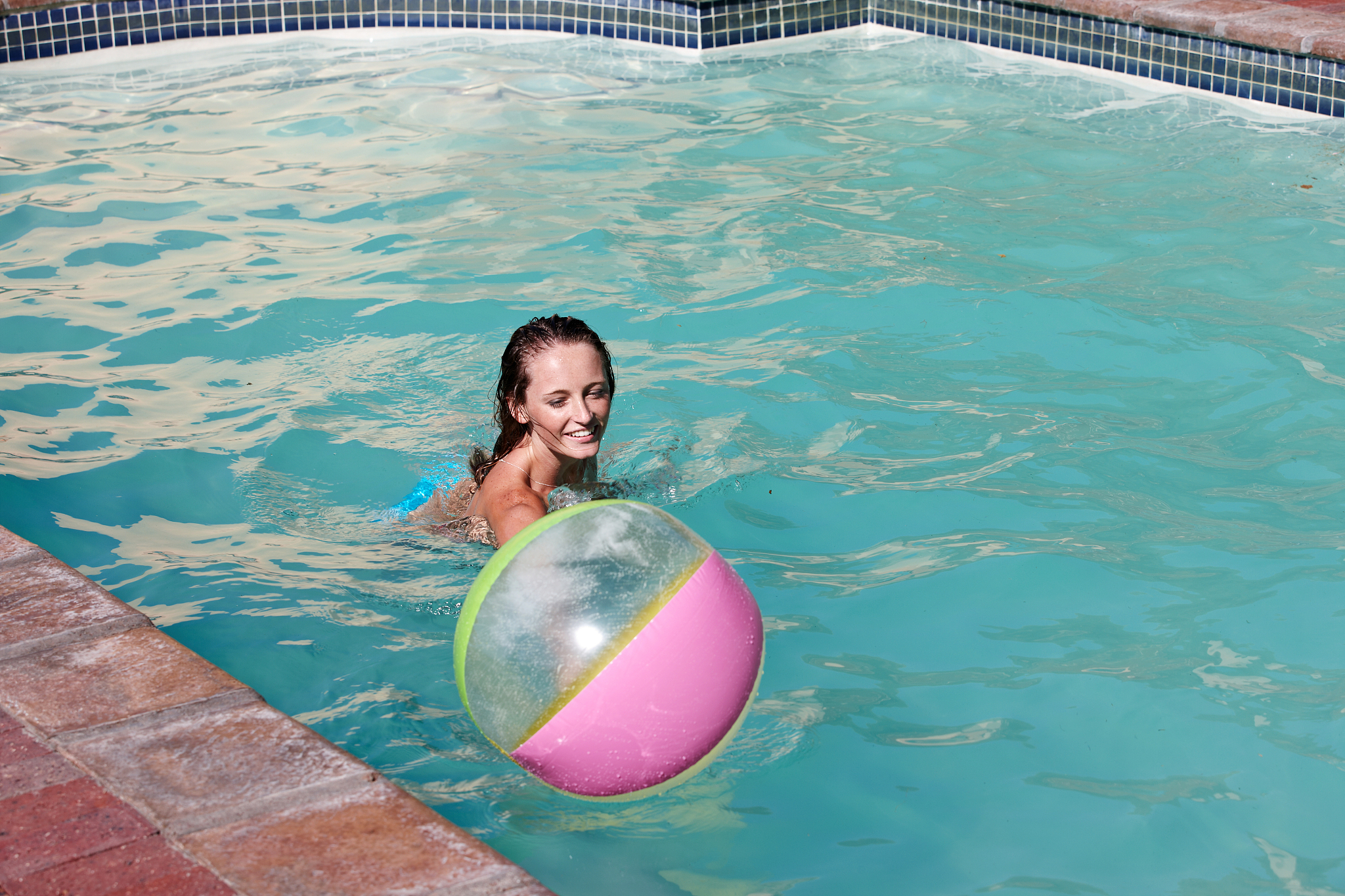 young female adult playing with beach ball in pool